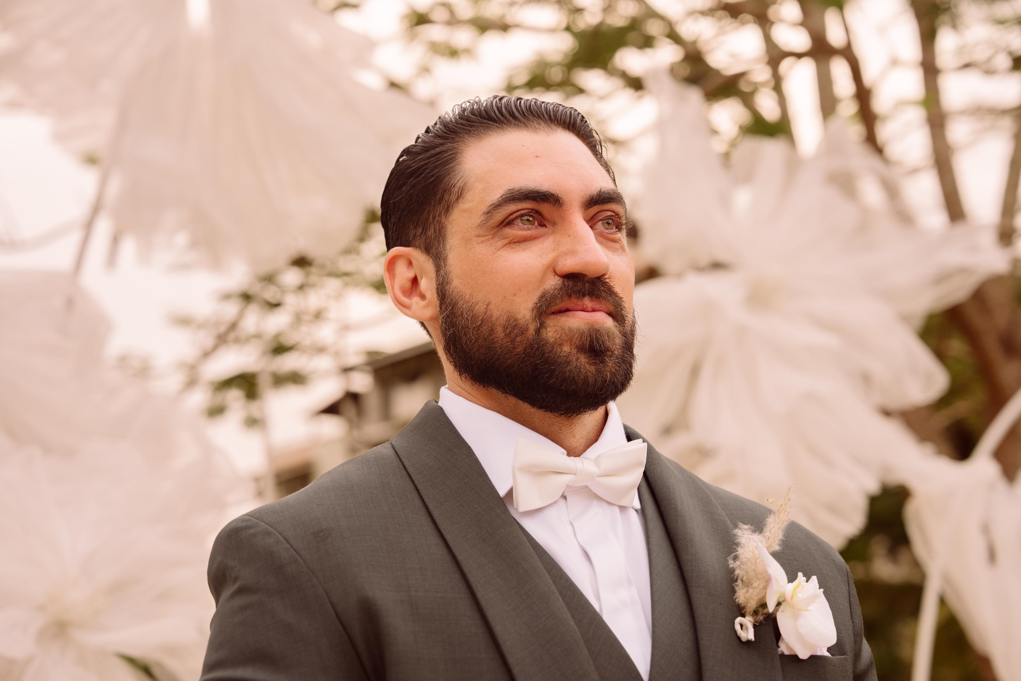 Man in a suit with a bow tie standing outdoors with decorative elements in the background