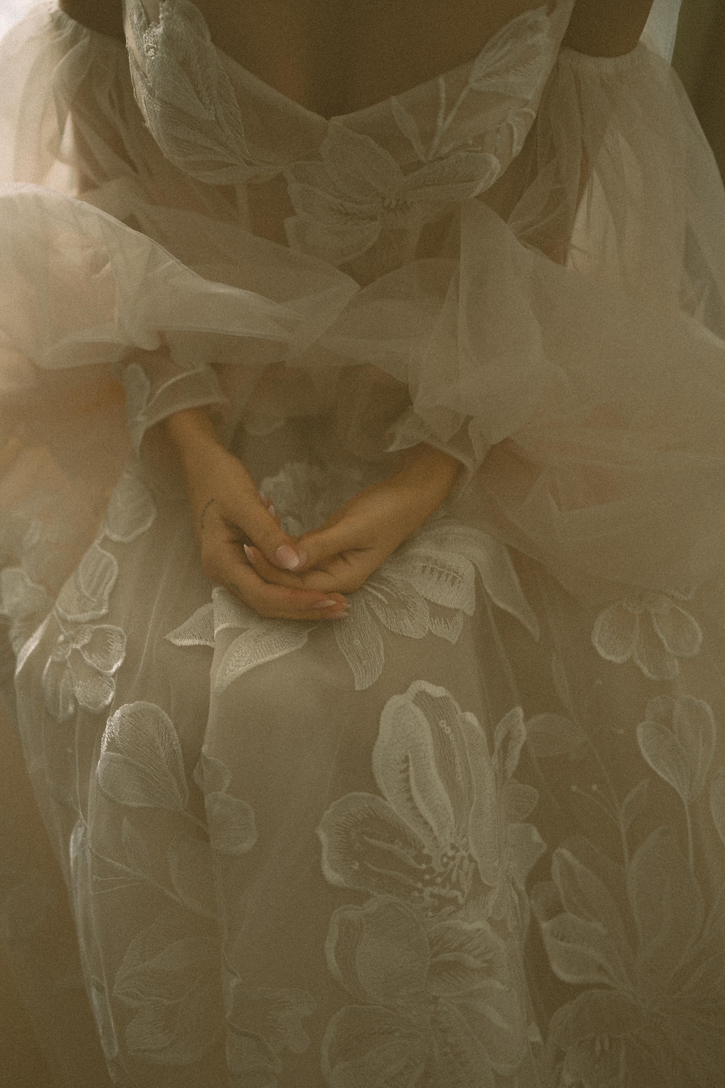 Close-up of  GL Bride Carina wearing the Evelyn wedding, sitting with hands clasped together.