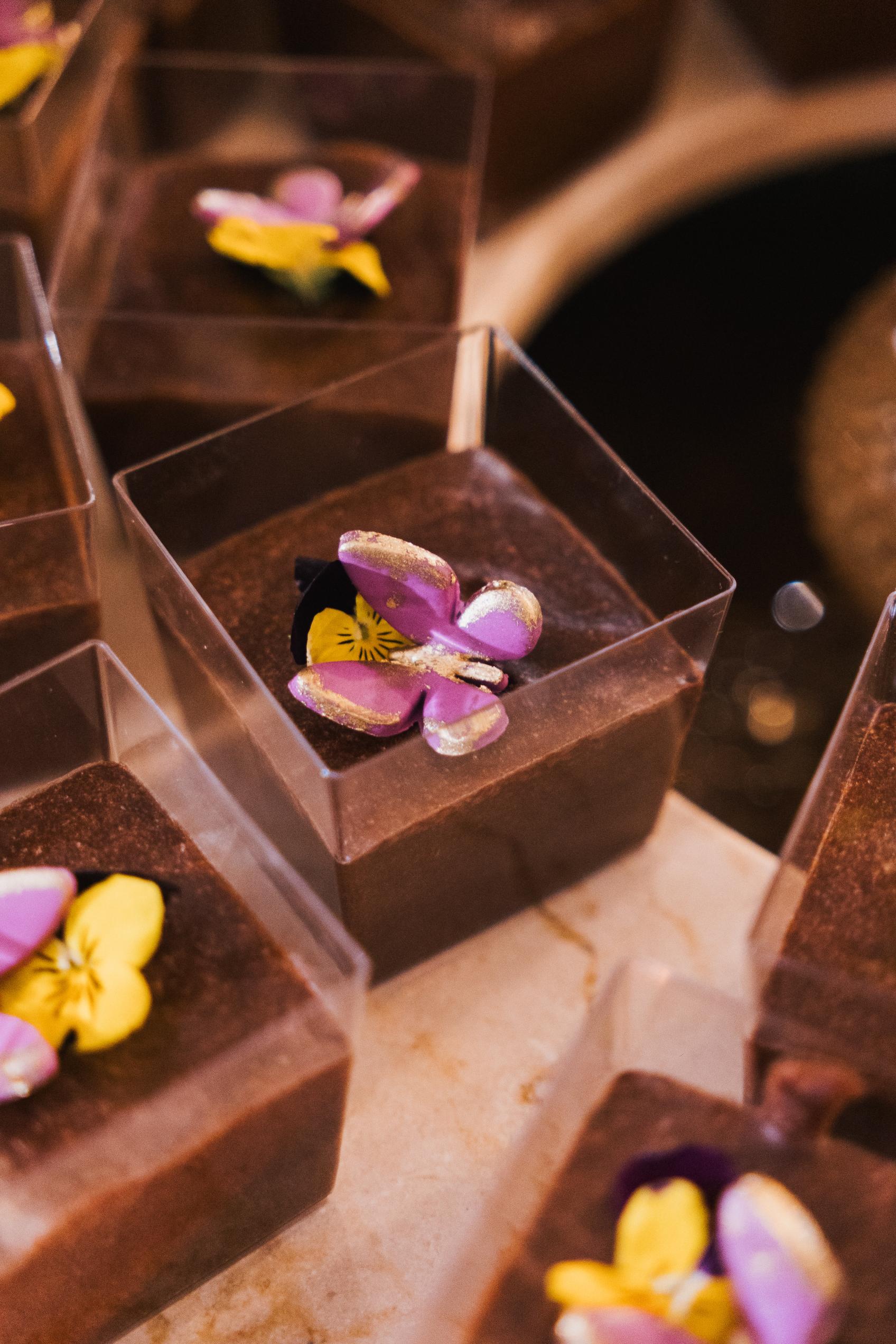 Chocolate desserts with floral toppings in clear containers on a marble surface.
