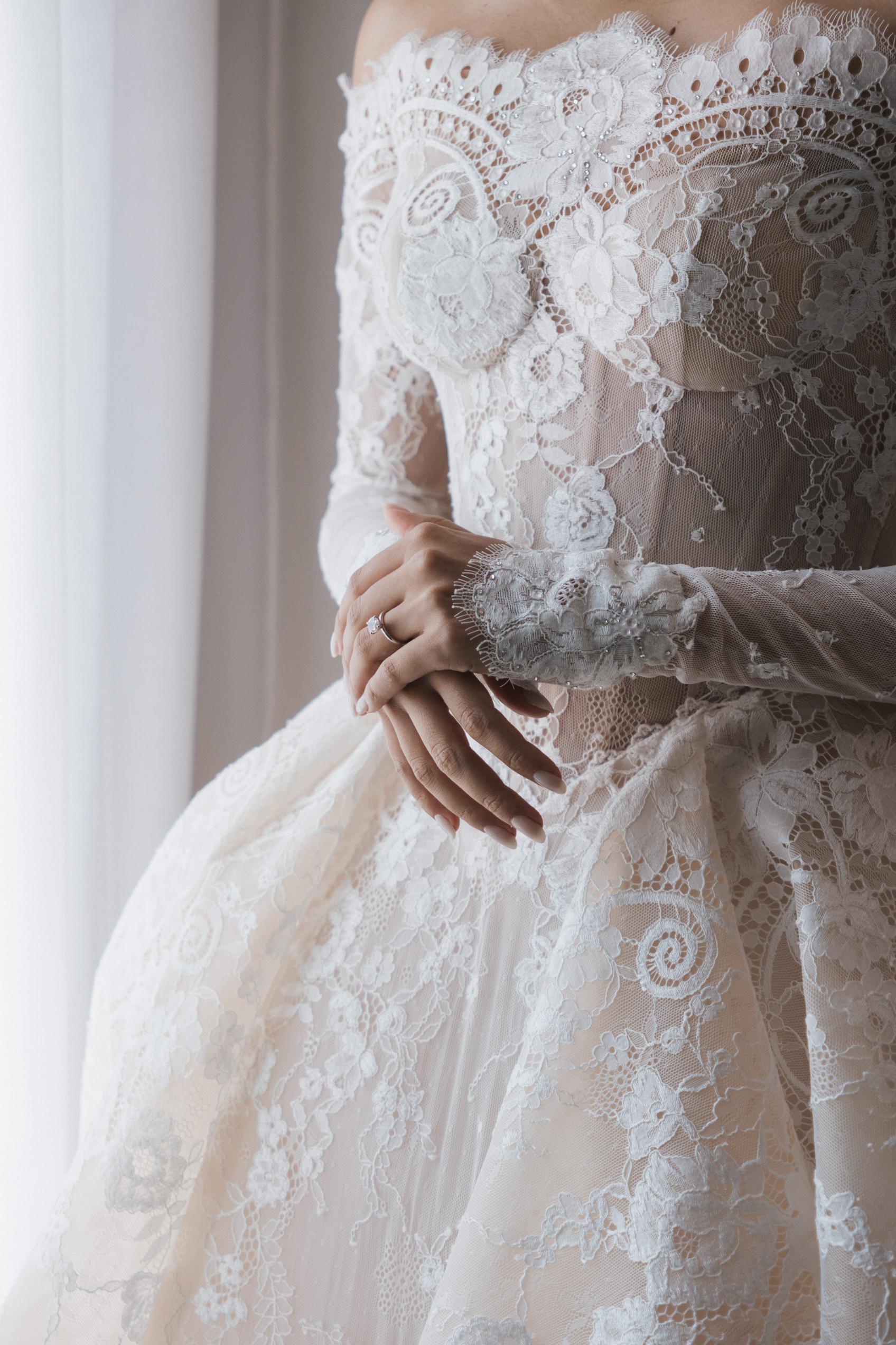 Close-up of a person wearing a detailed lace wedding dress with a blurred background