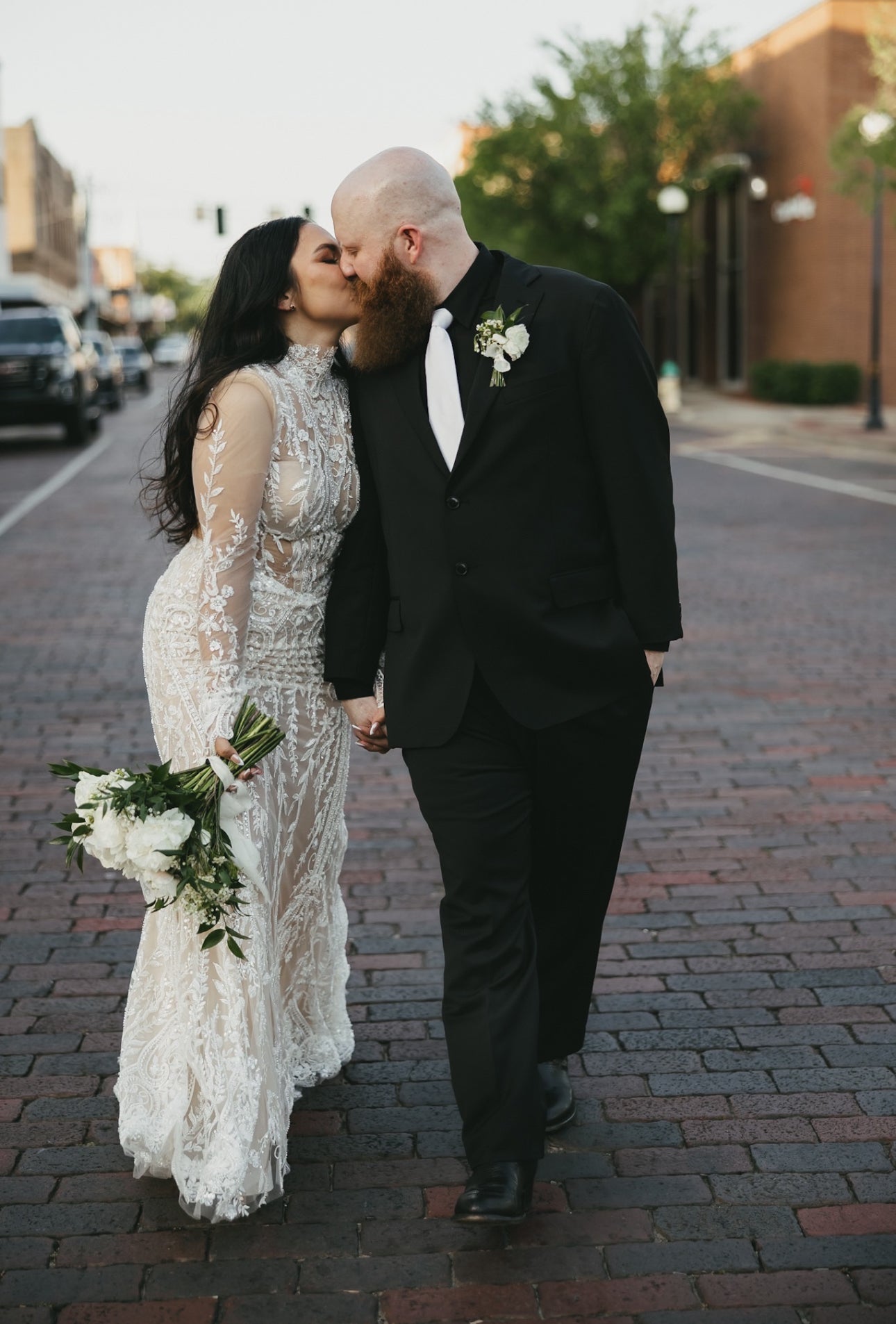 Couple in wedding attire walking on a brick street.