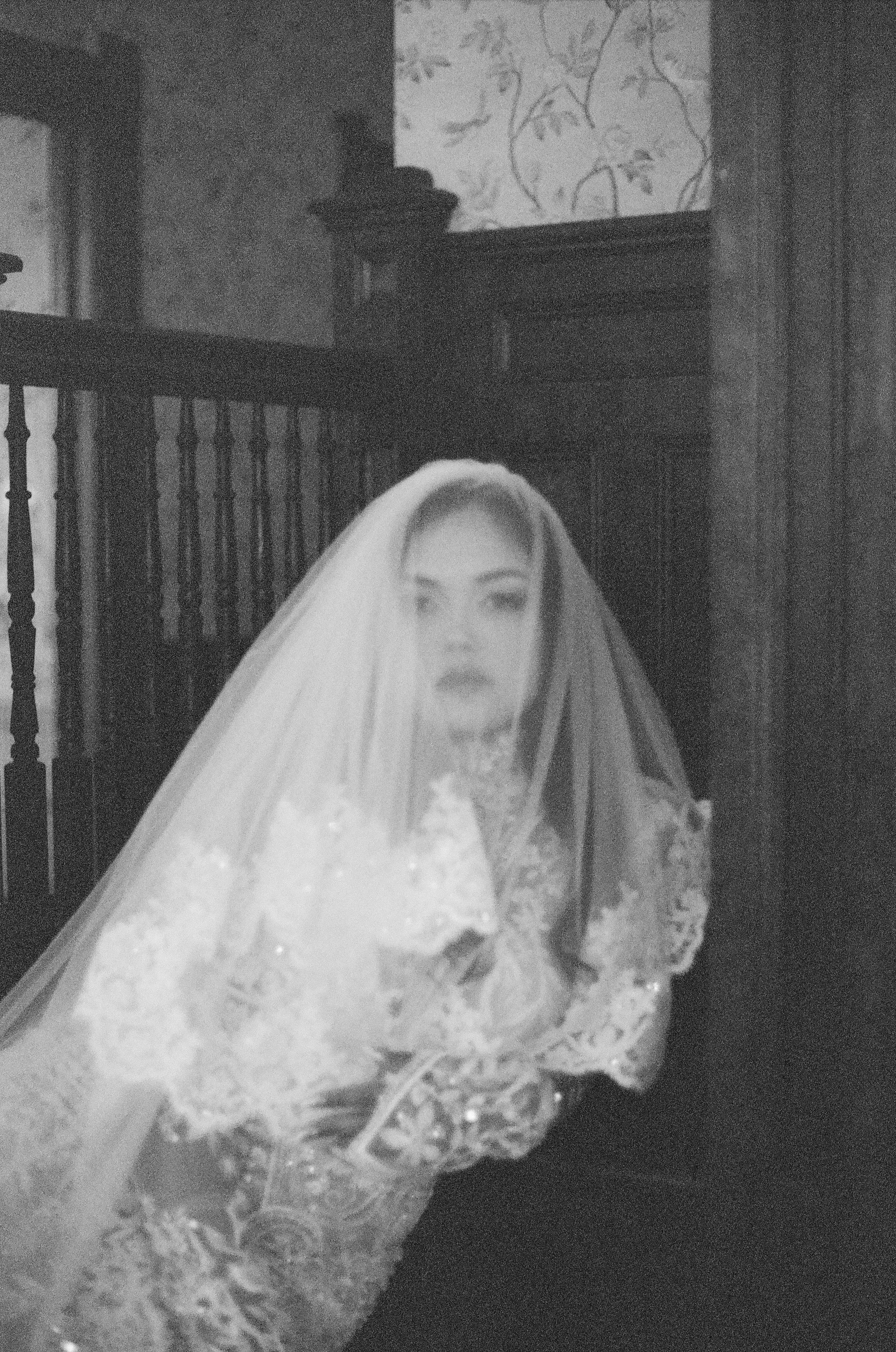 Black and white photo of a person wearing a wedding veil indoors.