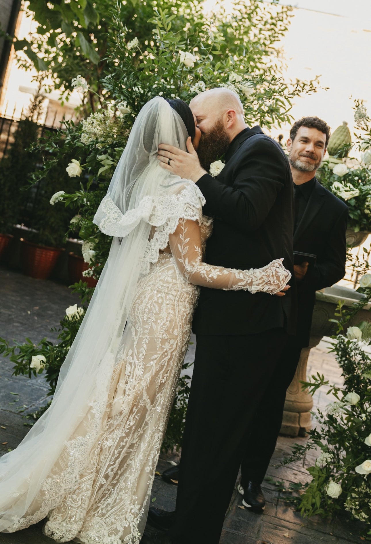 Couple in wedding attire embracing outdoors with floral decorations.