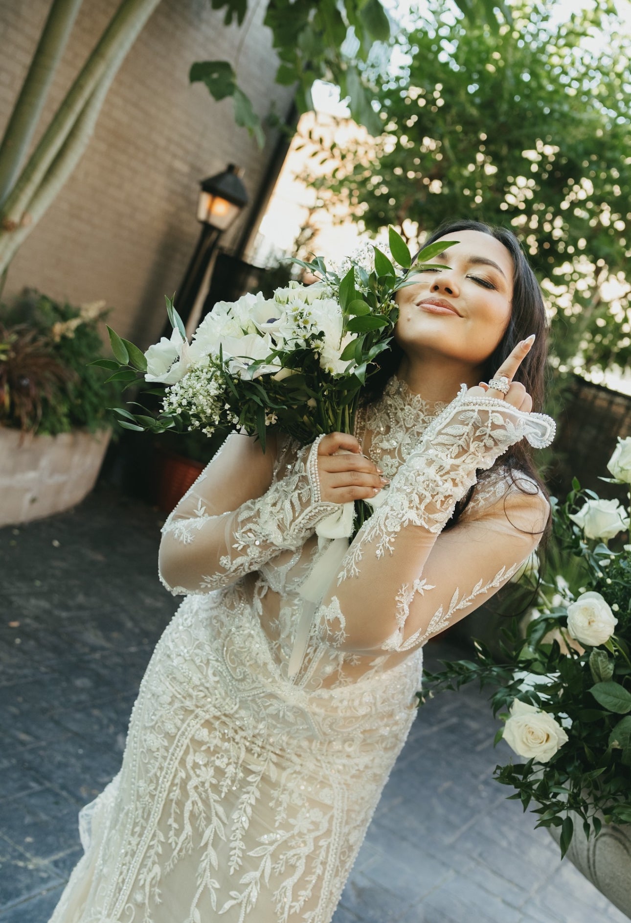 Woman in a lace wedding dress holding a bouquet of flowers outdoors.