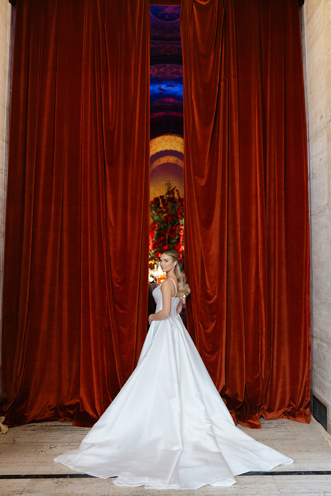 GL Bride Eliza wearing our Dove gown standing behind red curtain