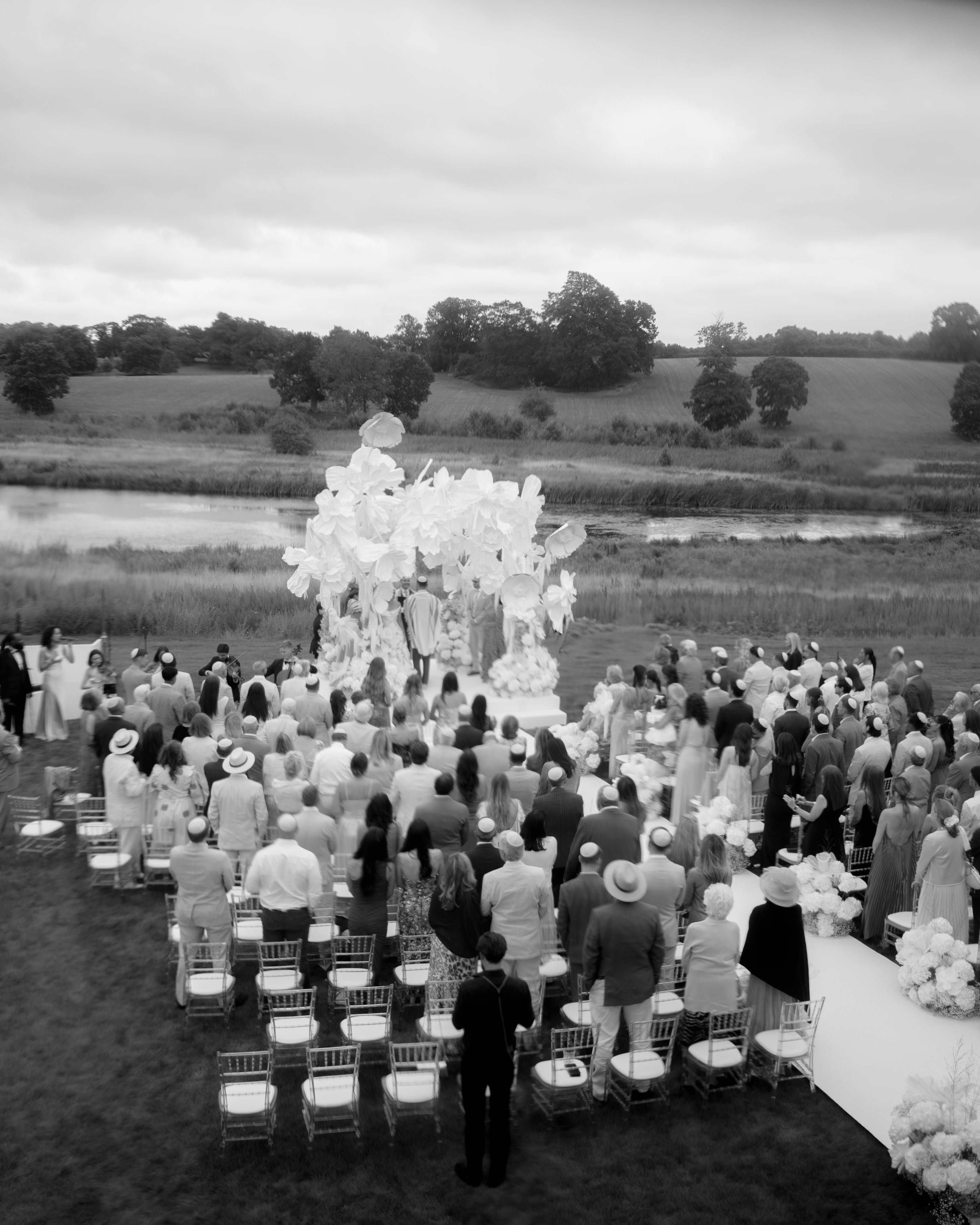 Outdoor wedding ceremony with guests and floral decorations by a lake.