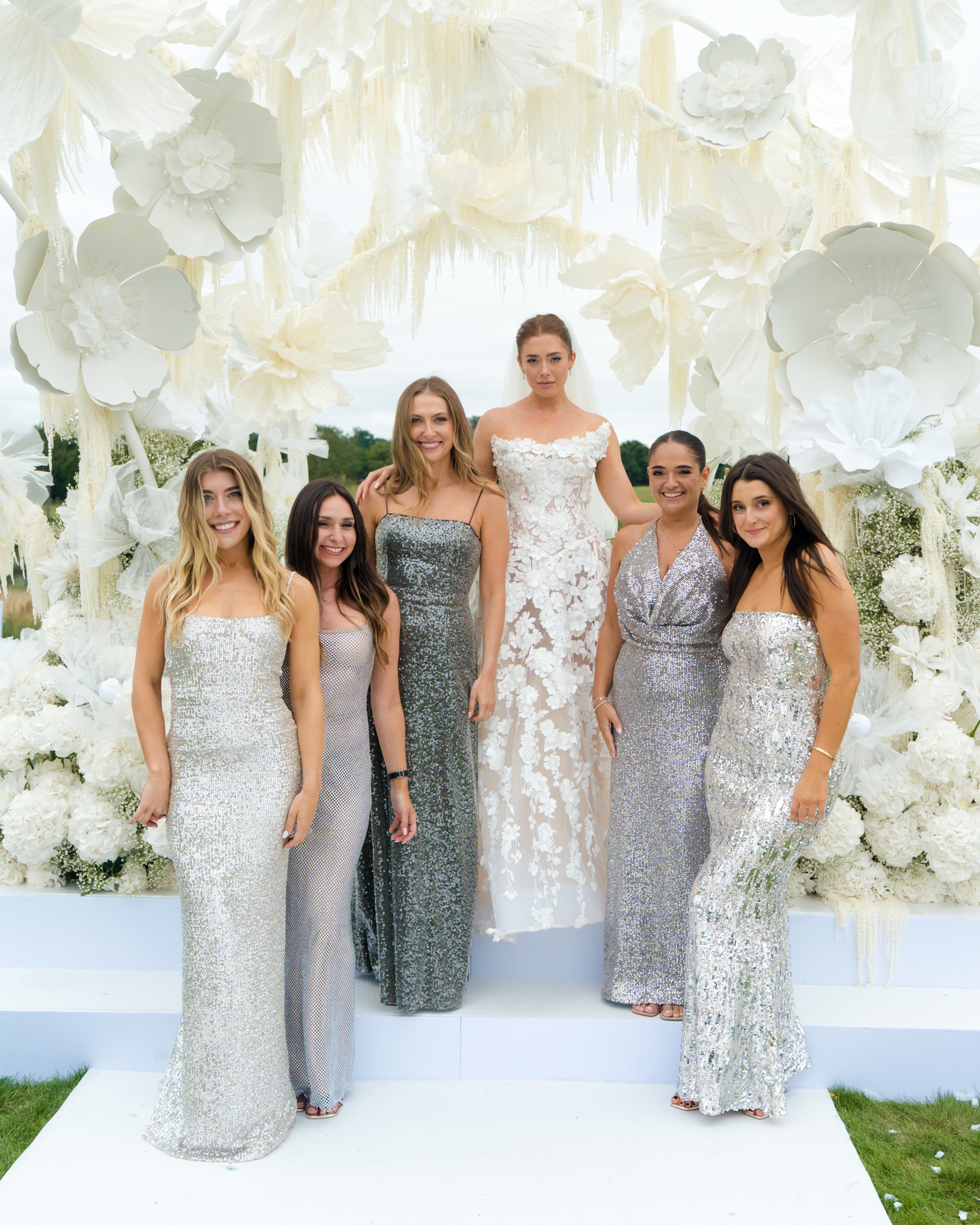 GL Bride Emily in our Rosemary and her bridesmaids standing in front of a floral backdrop