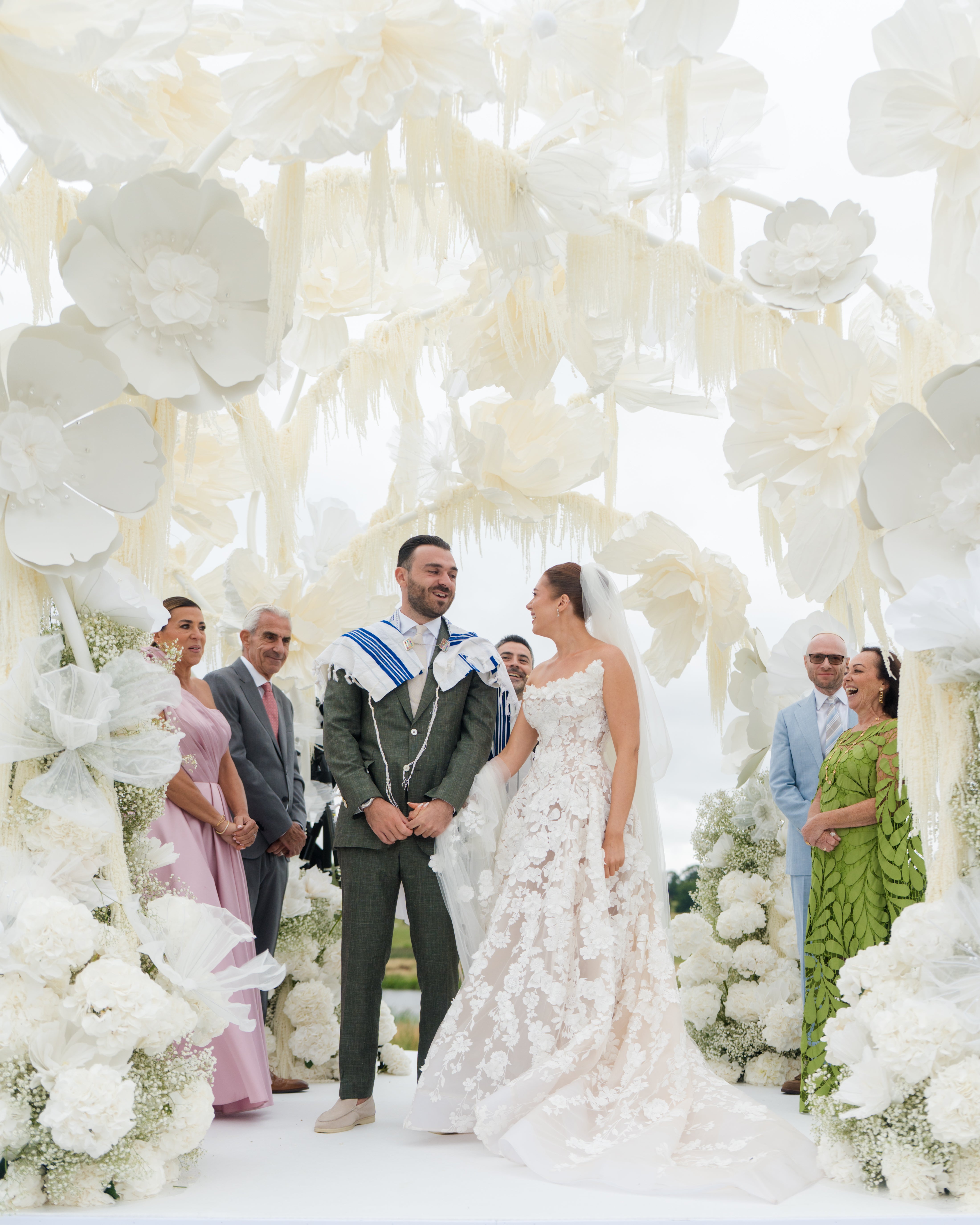 GL Bride Emily in our Rosemary and her husband standing under a floral archway with guests in formal attire.
