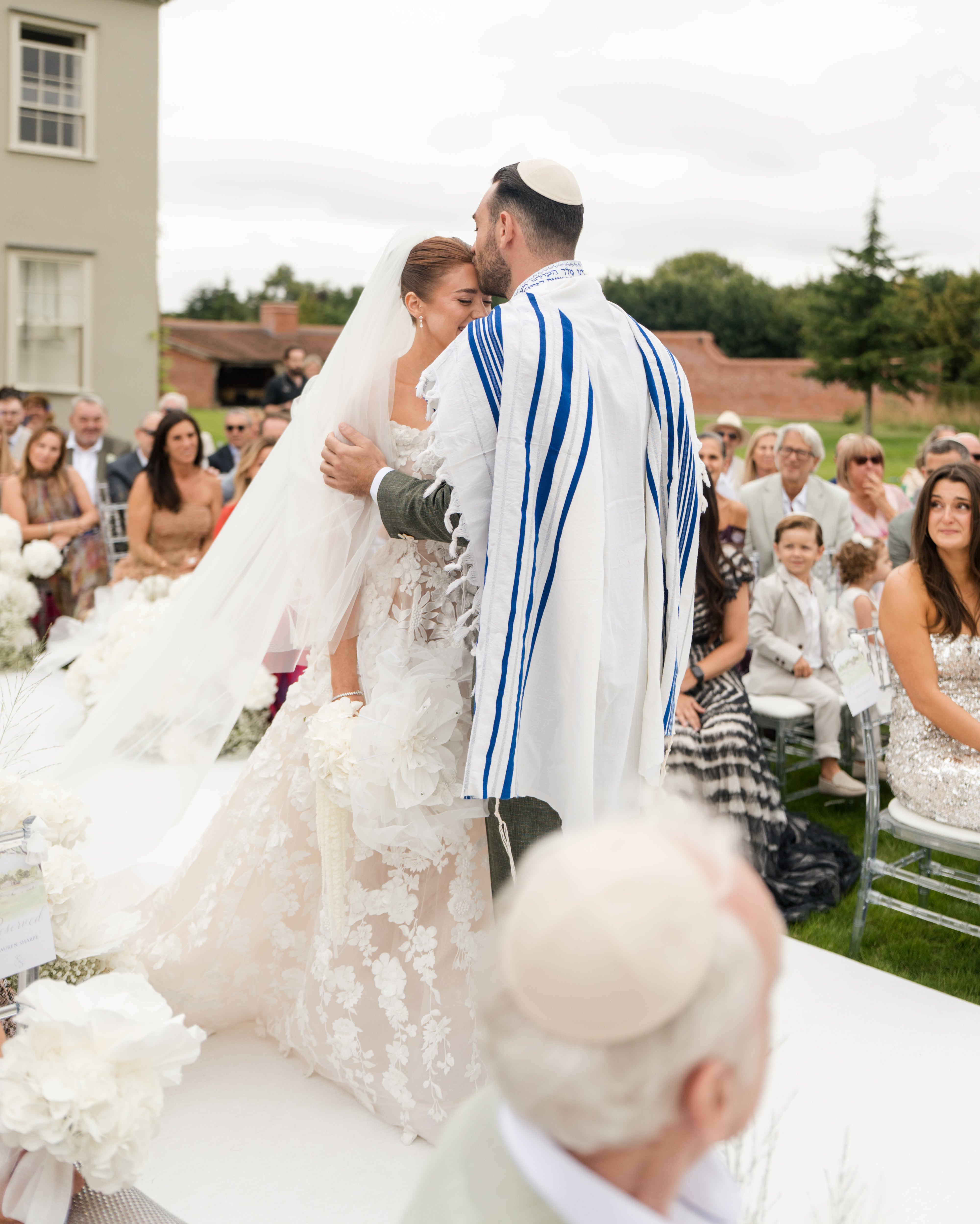 Wedding ceremony of GL Bride Emily in our Rosemary gown, surrounded by guests outdoors.