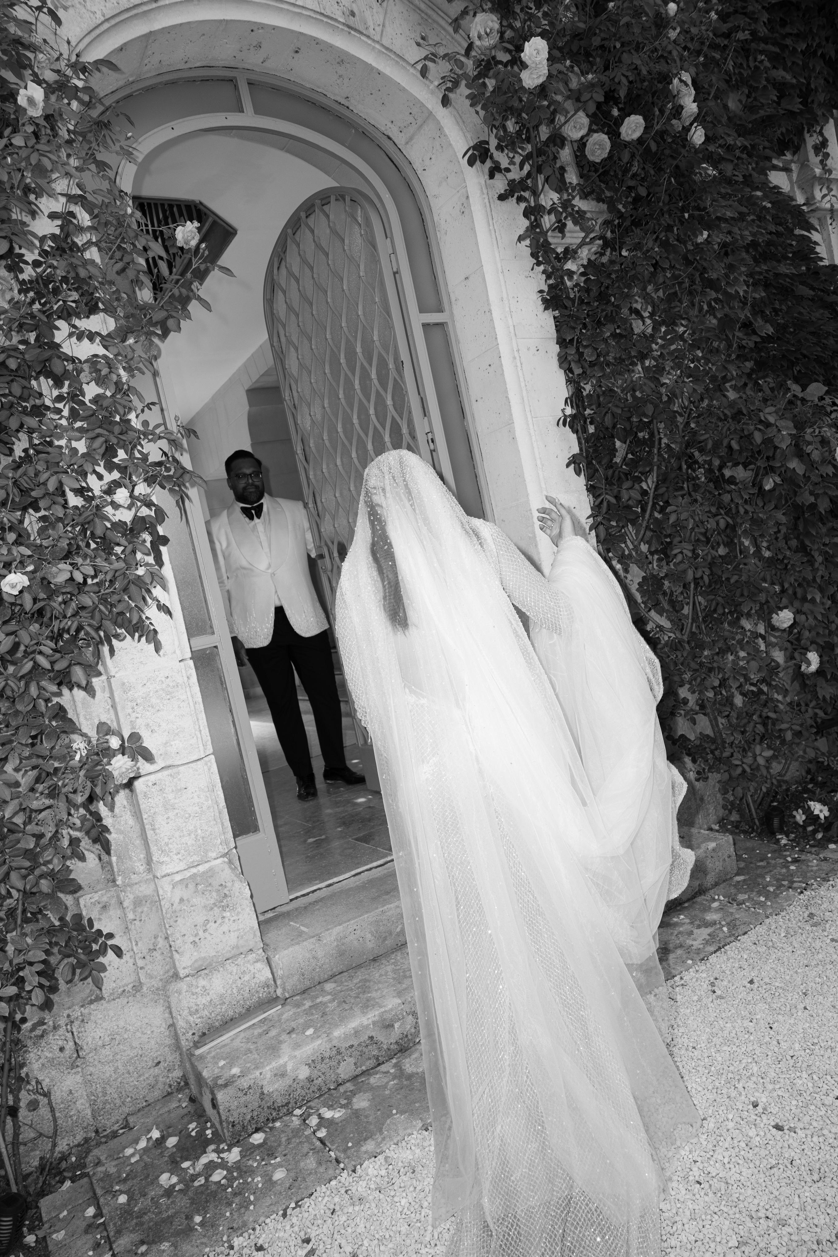 Black and white photo of a bride and groom with a man in a suit standing in a doorway.