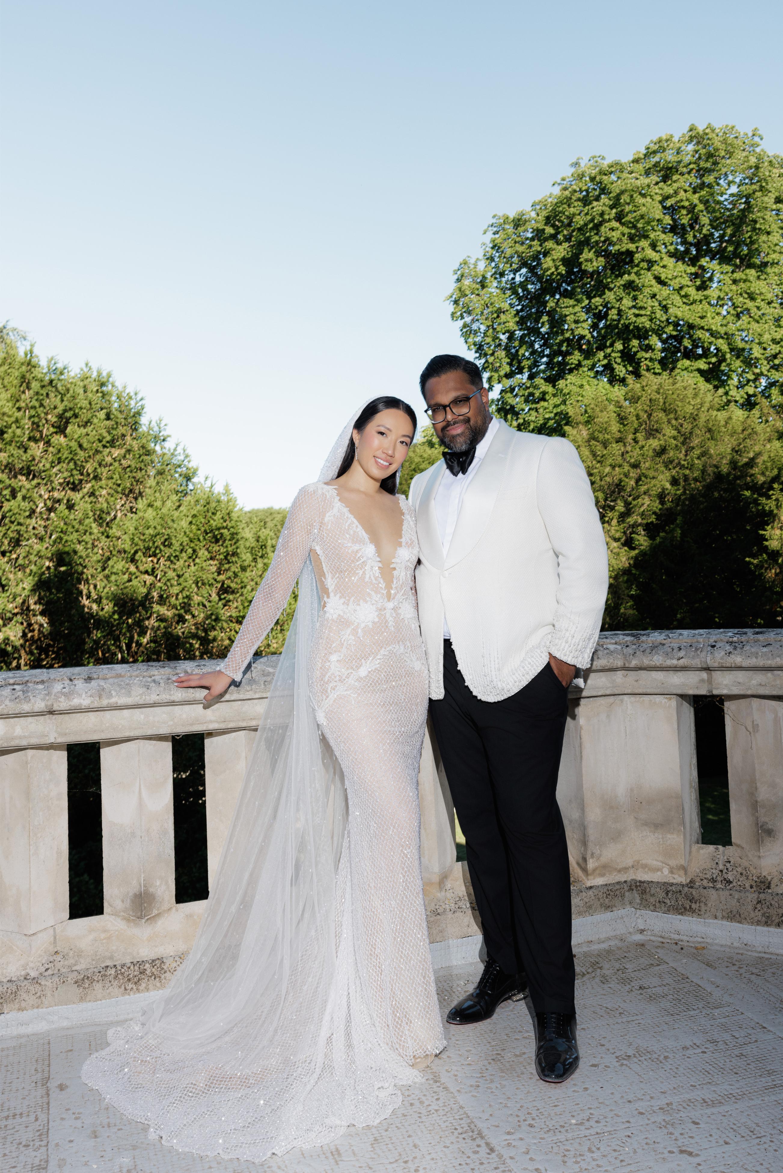 Man and woman in formal attire standing on a balcony with trees in the background