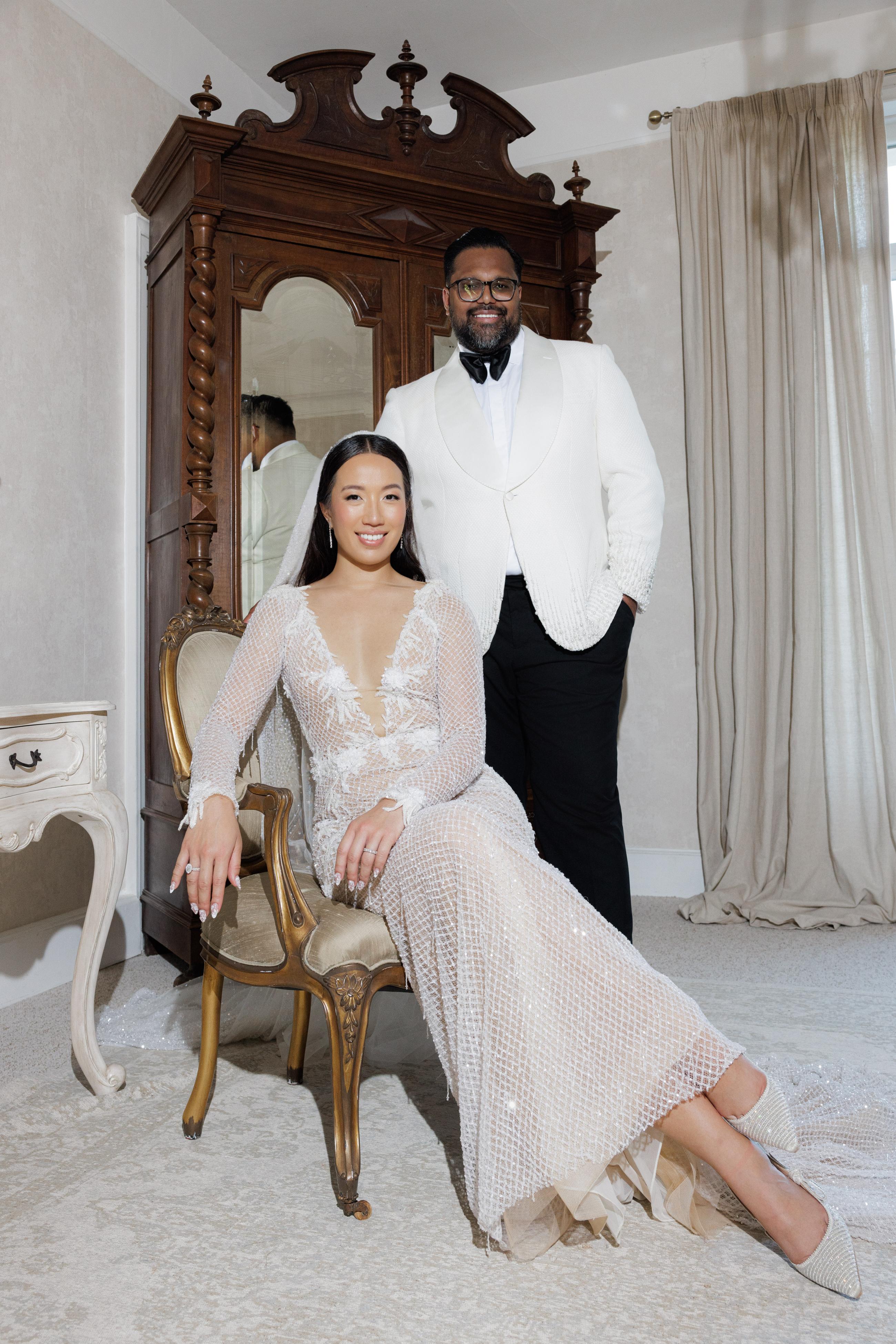Man and woman in formal attire posing in a room with an ornate wooden cabinet.