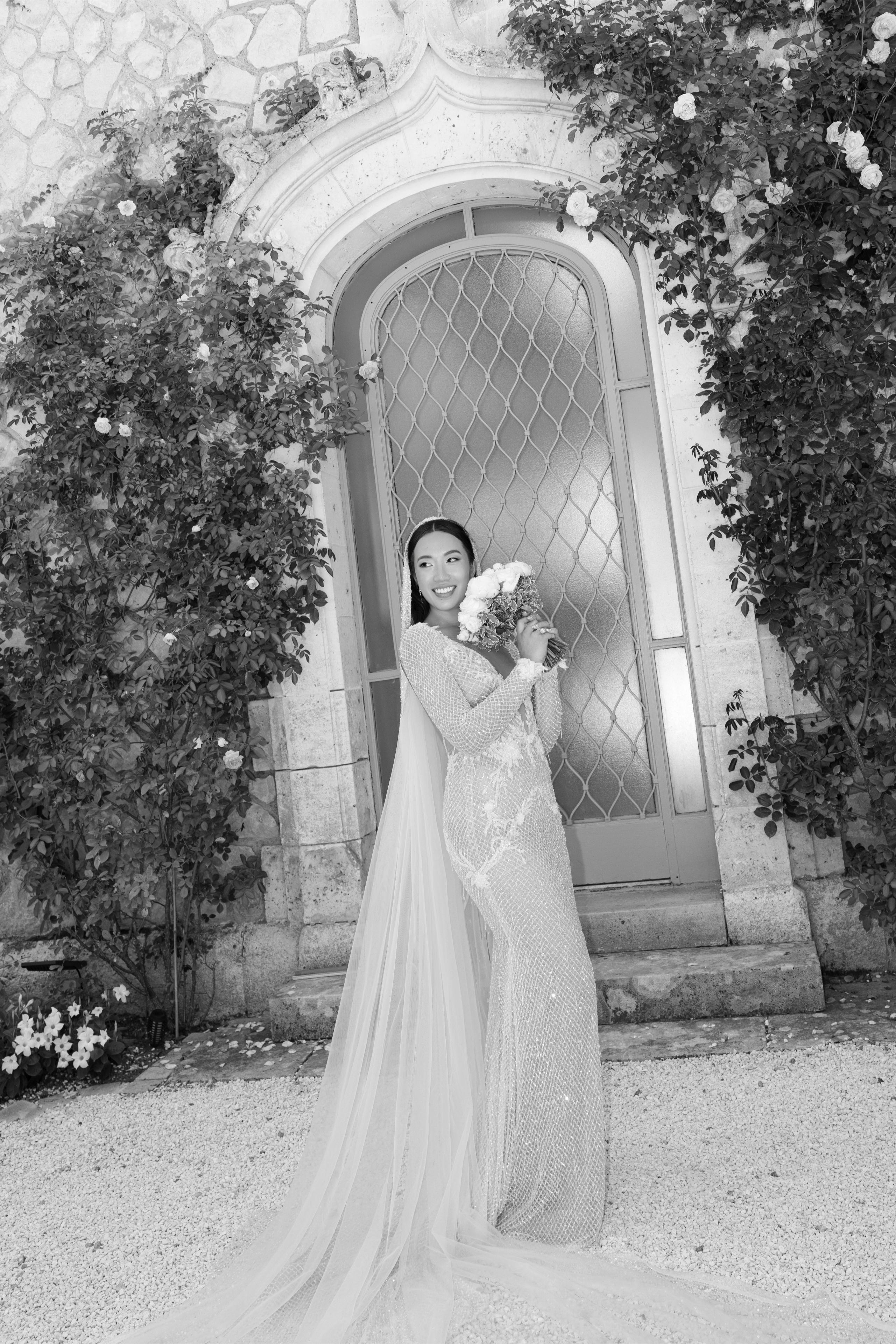 Woman in a wedding dress holding flowers in front of an ornate door with floral decorations.