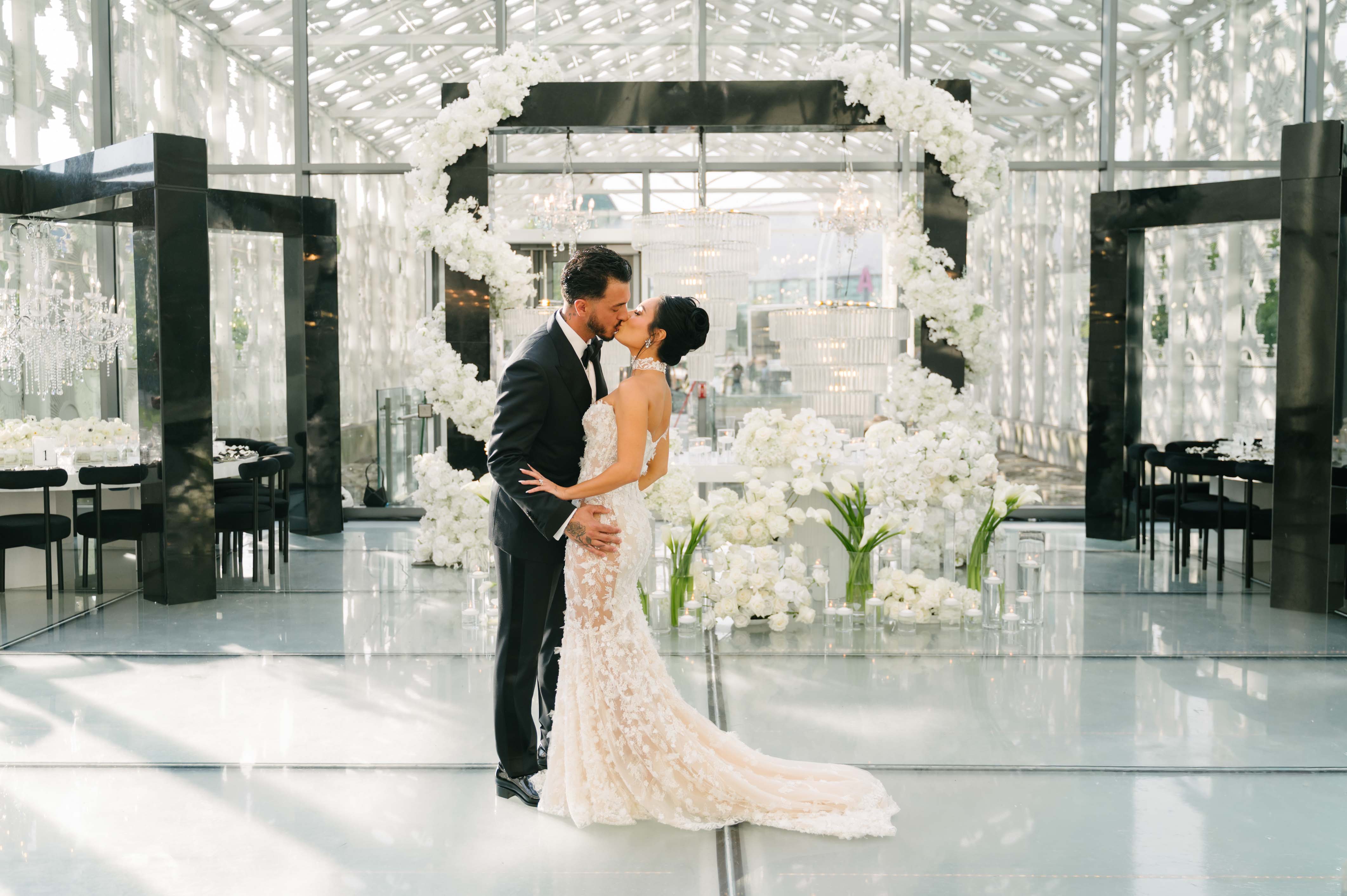 Couple kissing in a modern indoor setting with white floral arrangements.