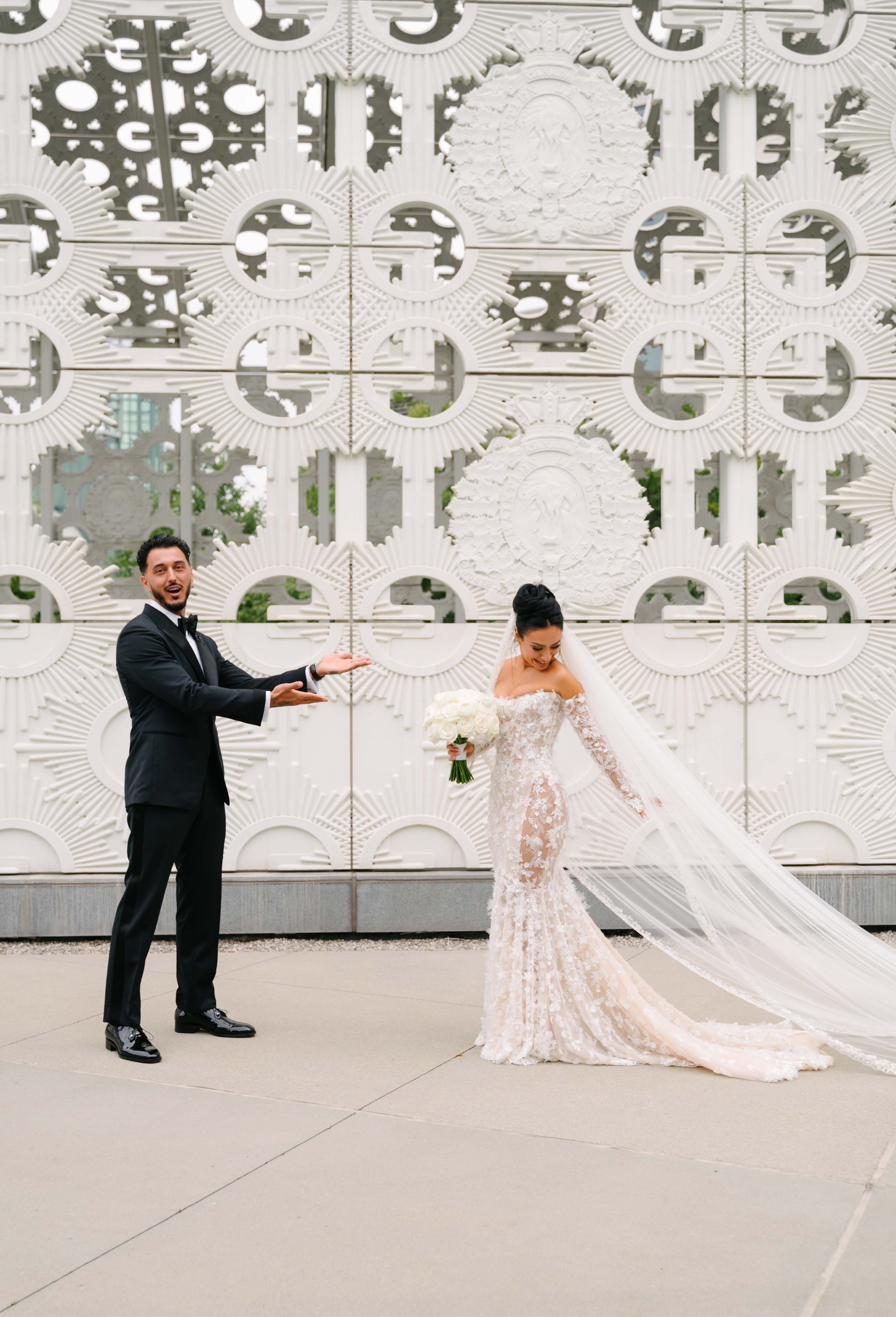 GL Bride Eva in our Maya and her husband posing in front of a decorative wall.
