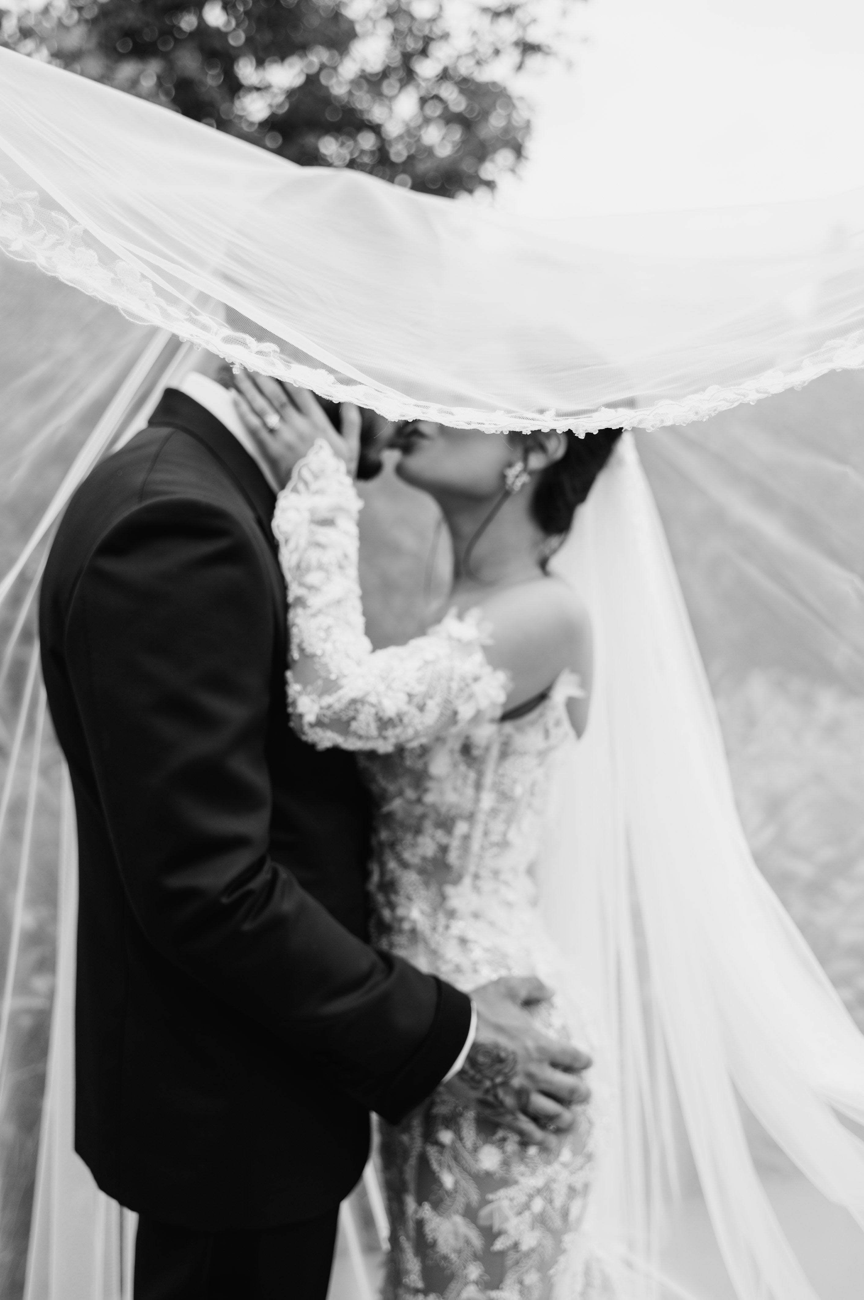 Black and white photo of a GL Bride Eva and her husband kissing under a veil.
