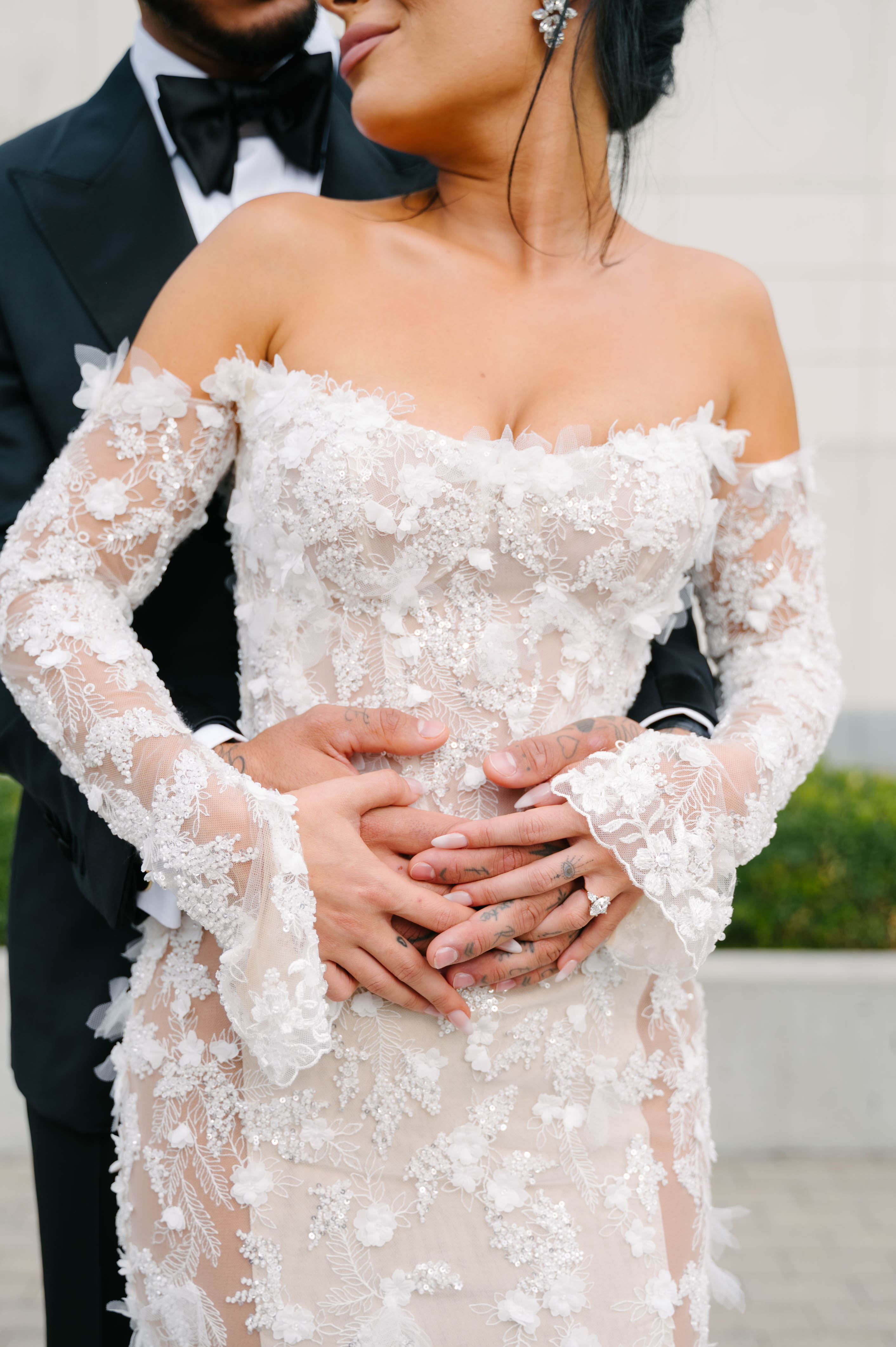 GL Bride Eva in a custom Maya dress holding hands with her husband wearing a suit, blurred background