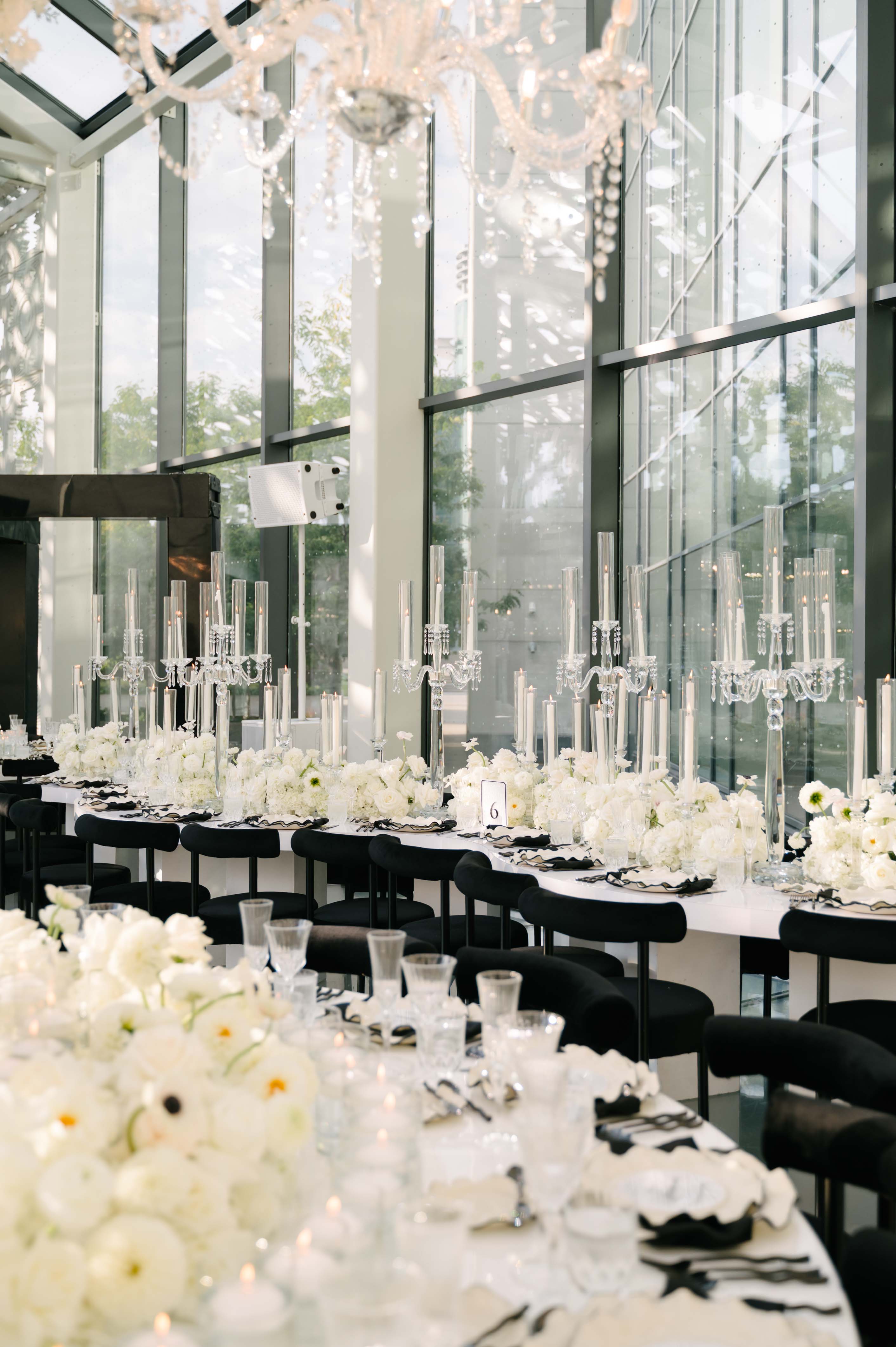 Elegant indoor setting with tables set for a formal event, featuring white flowers and crystal candle holders.