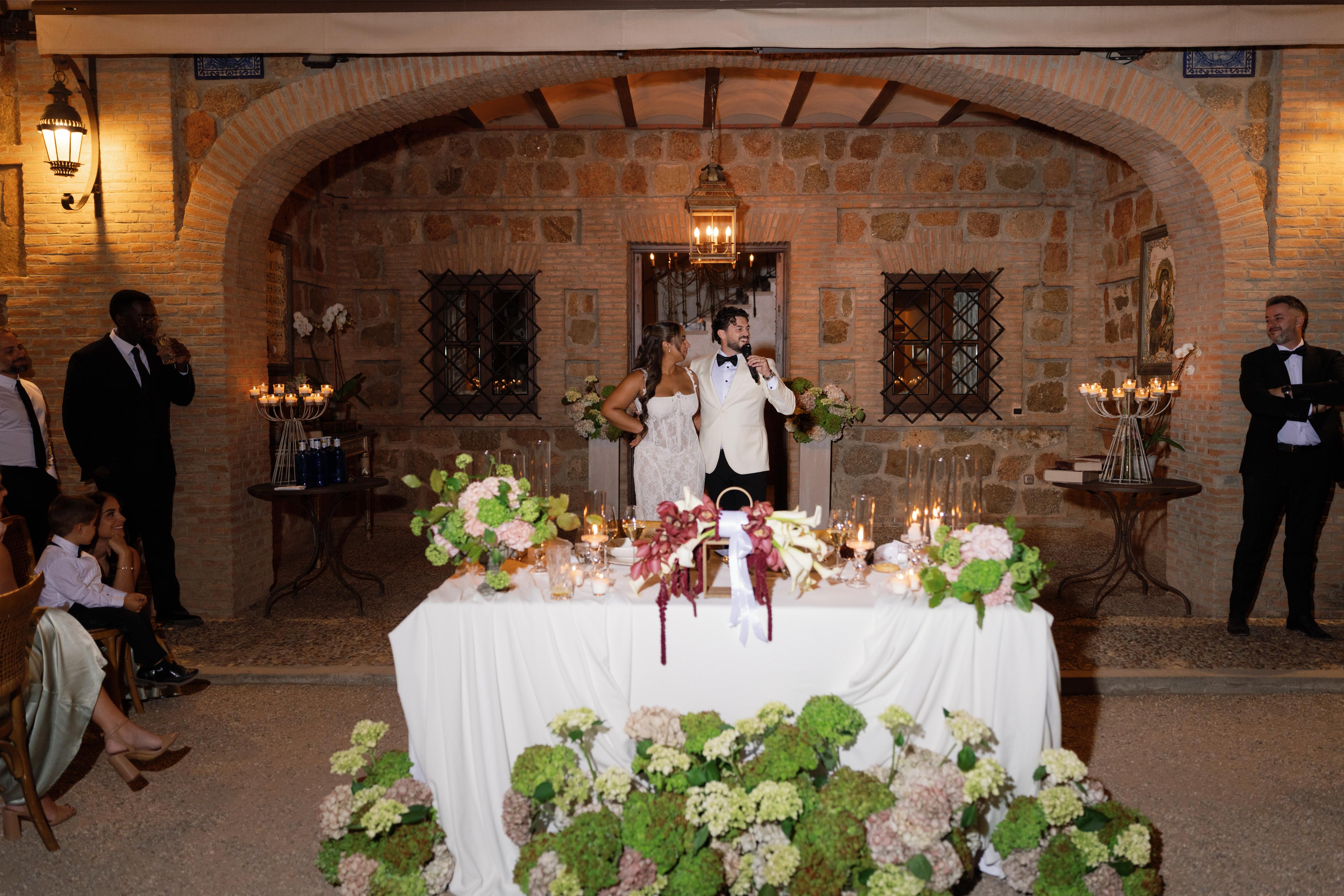 Wedding reception with a couple at a decorated table in a rustic stone-walled room.