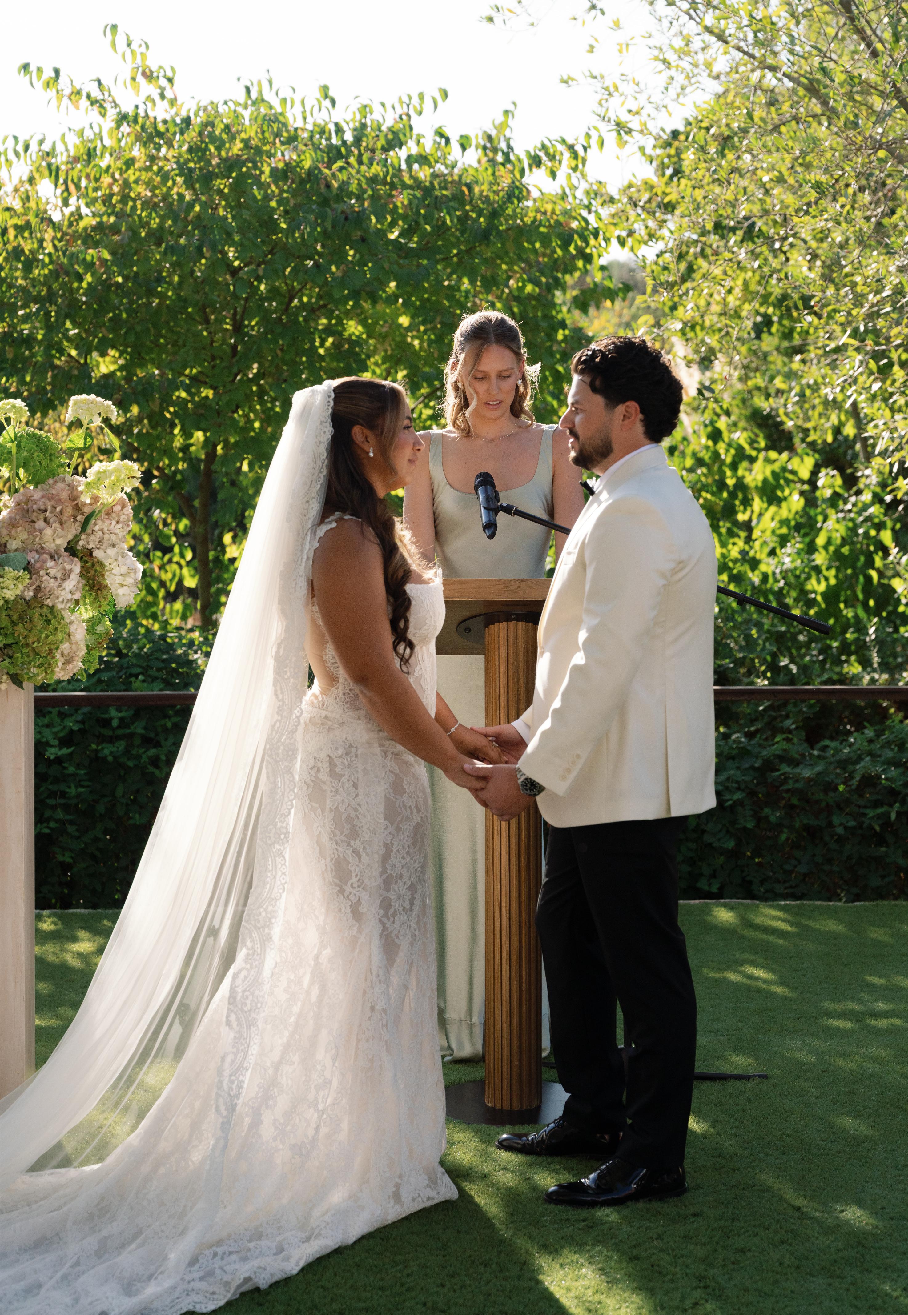 Wedding ceremony with GL Bride Janai in our Anais and her groom, and the officiant outdoors.