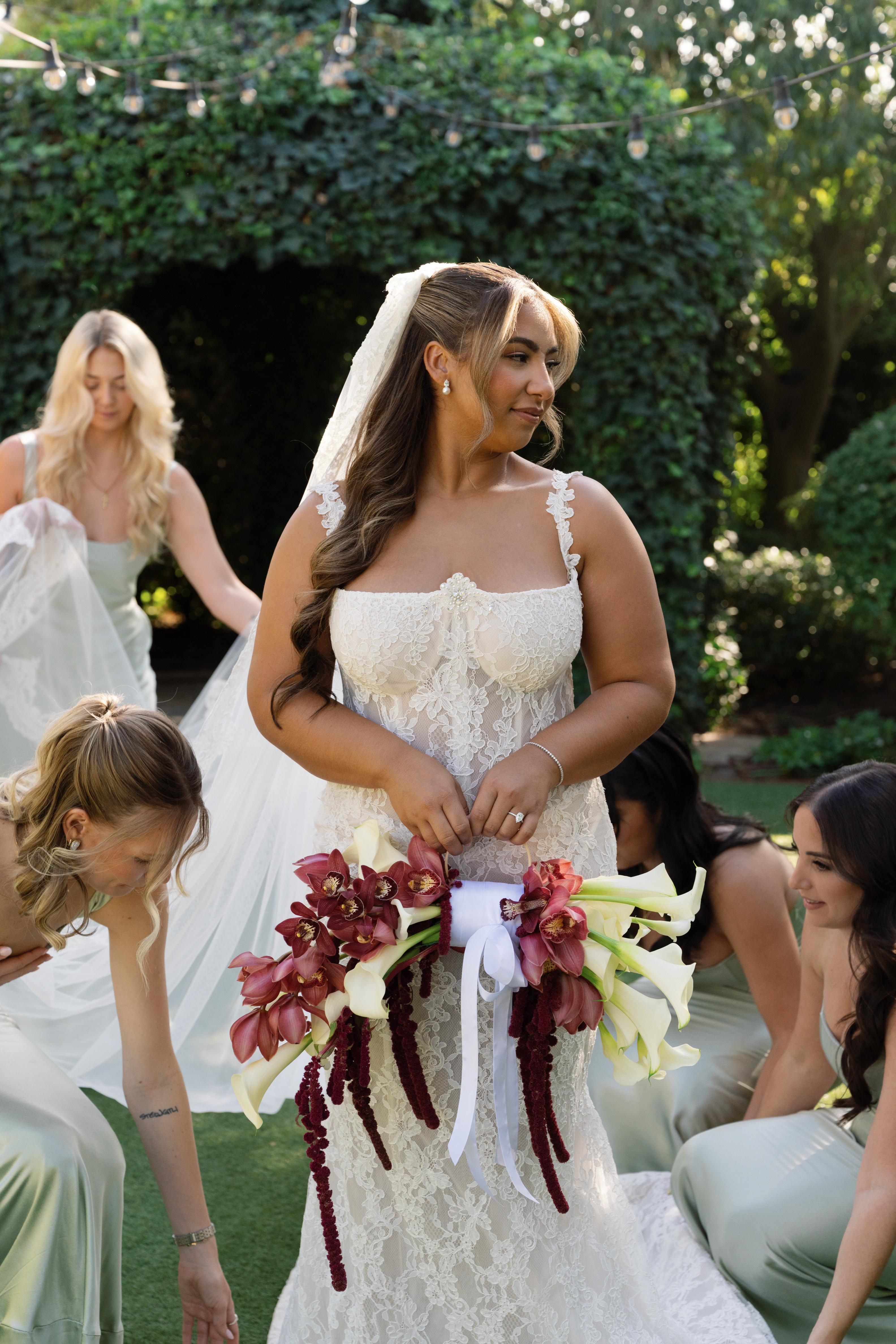 GL Bride Janai in our Anais  holding a bouquet with her bridemaids surrounding her outdoors.