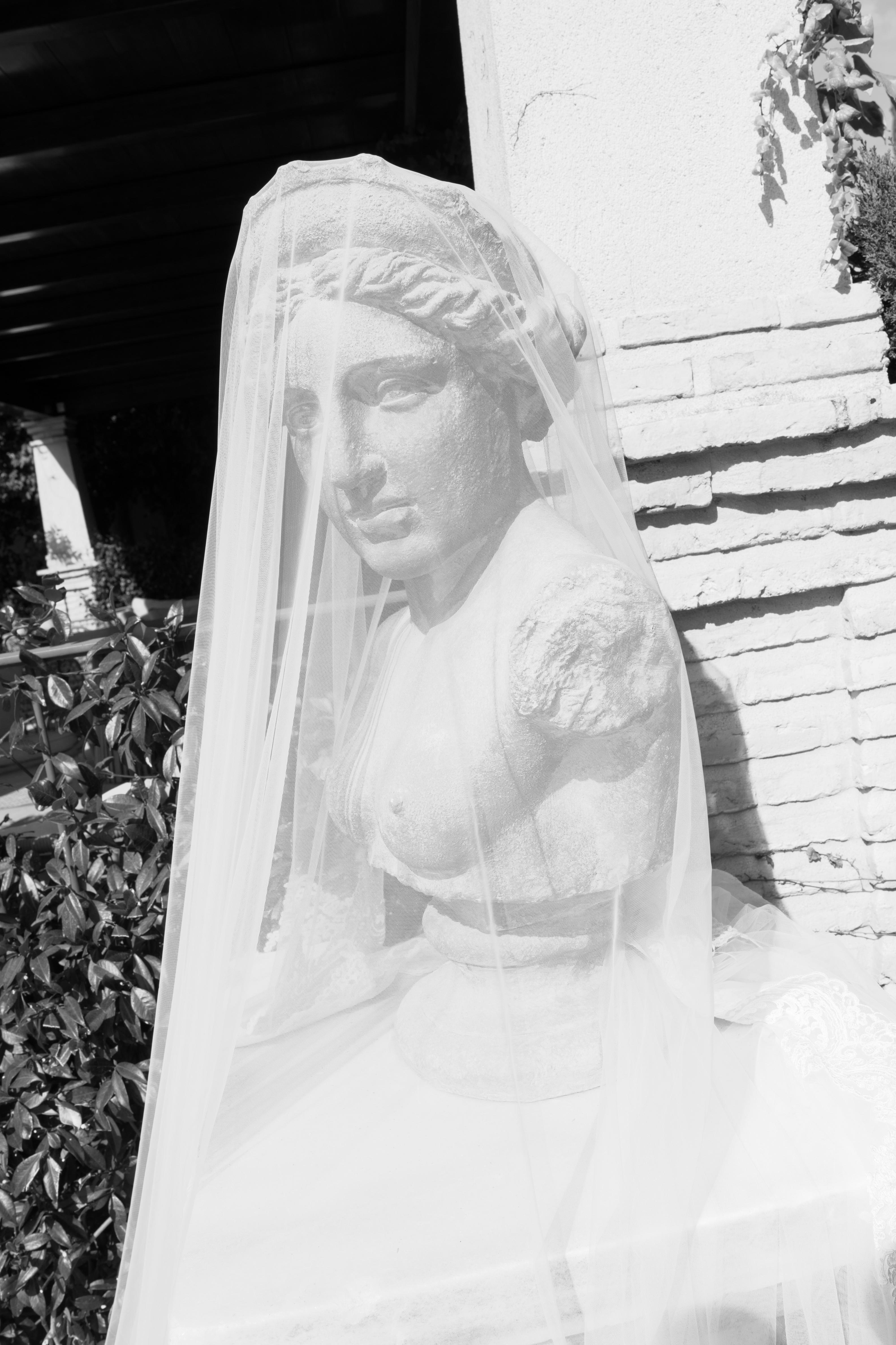 Statue of a woman in a veiled gown against a textured wall.