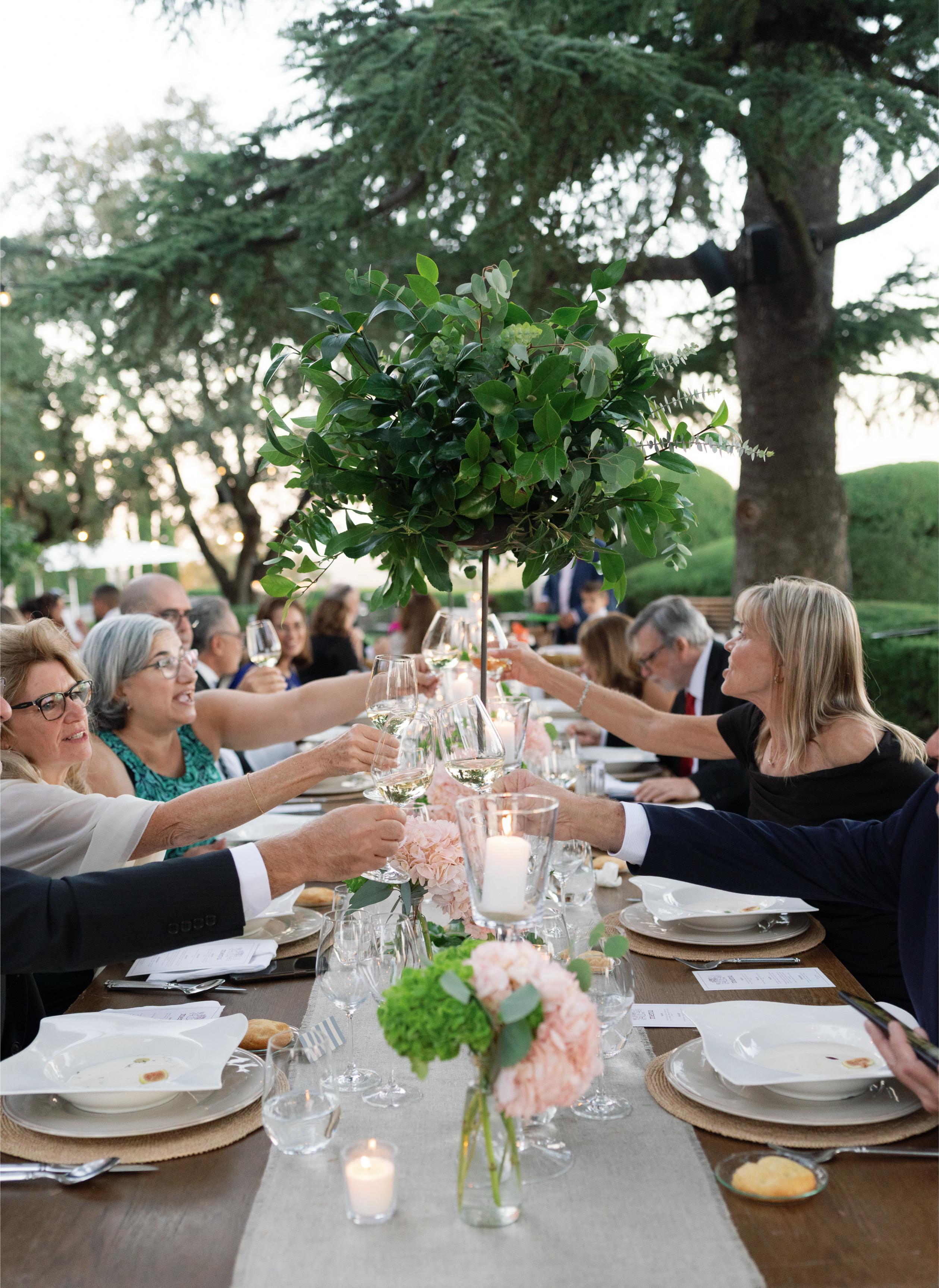 People at a dinner table outdoors with greenery and trees in the background