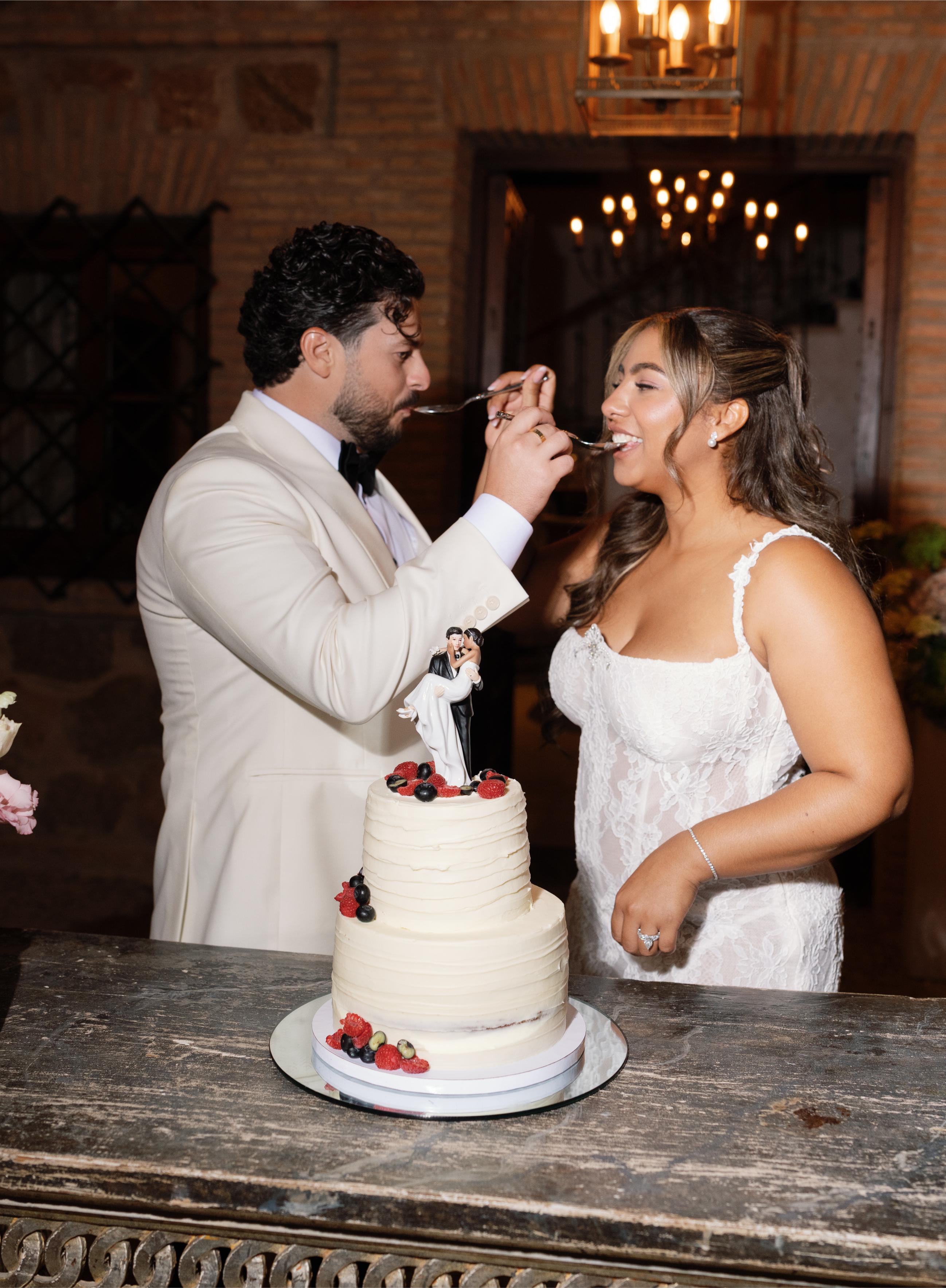 GL Bride Janai in our Anais  and her husband feeding each other cake at a wedding reception.
