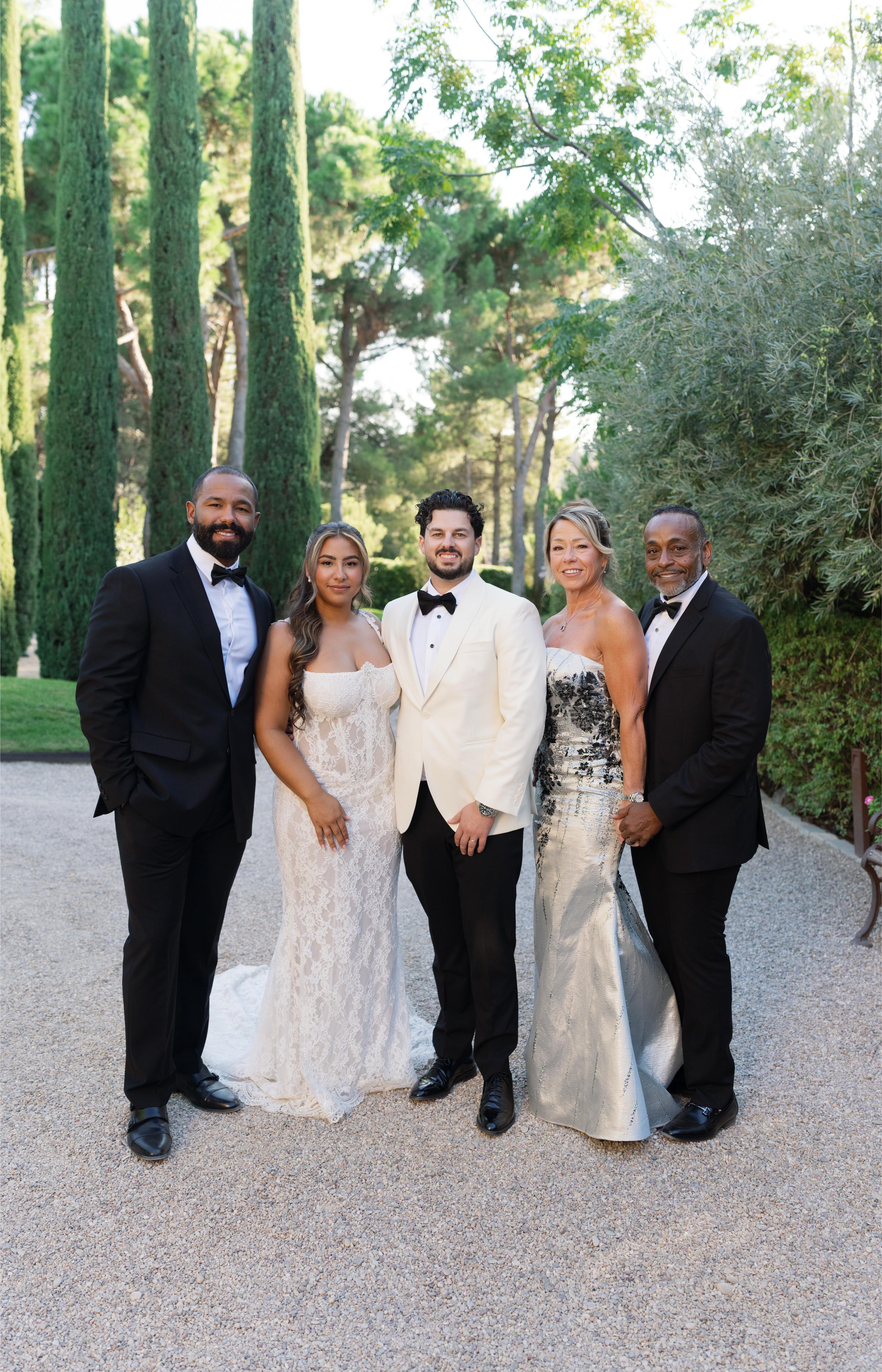 Our GL Bride Janai in Anais standing with her husband and family outdoors with trees in the background
