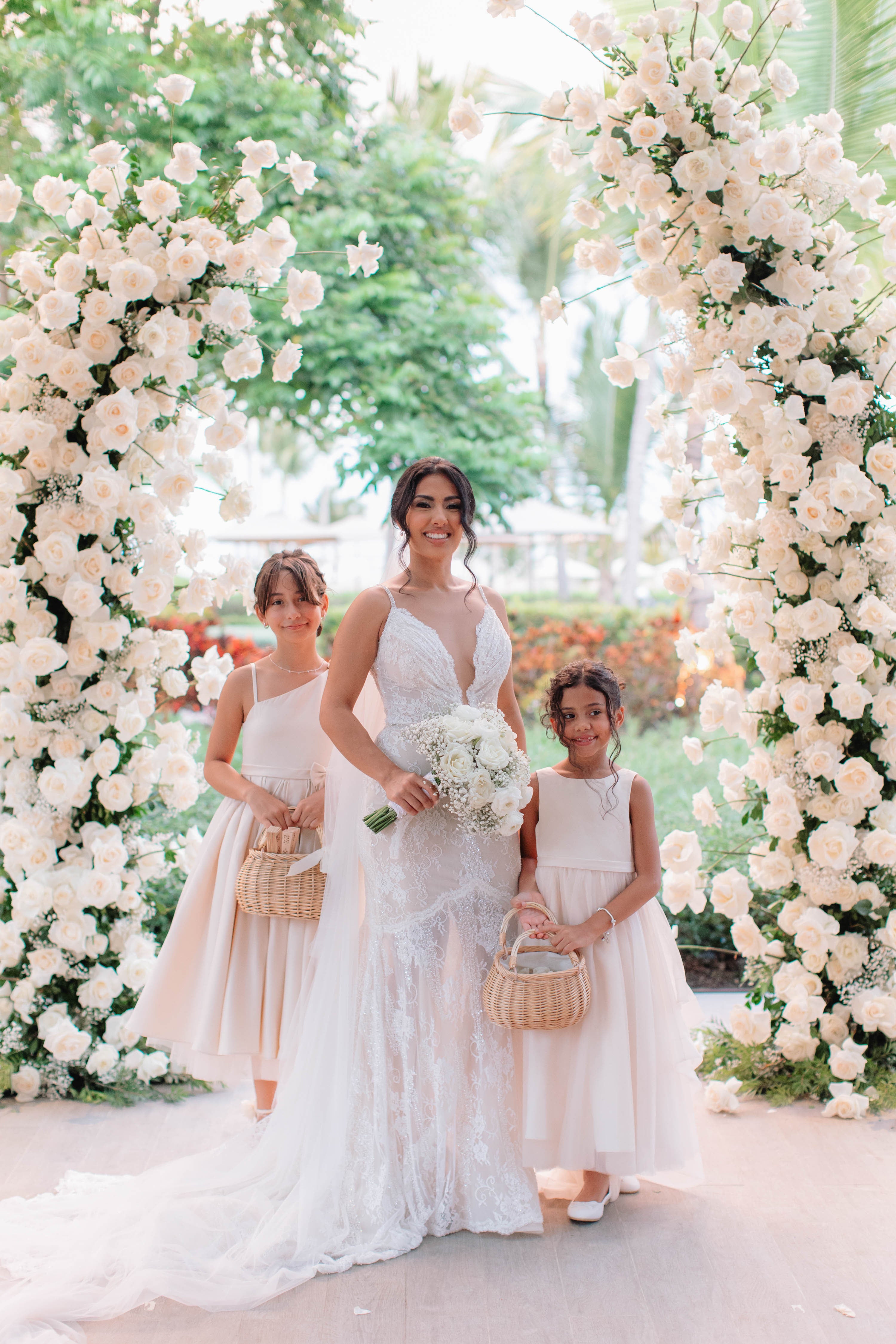 GL Bride Jennifer wearing our G-404 standing between two young girls with floral arrangements in a garden setting