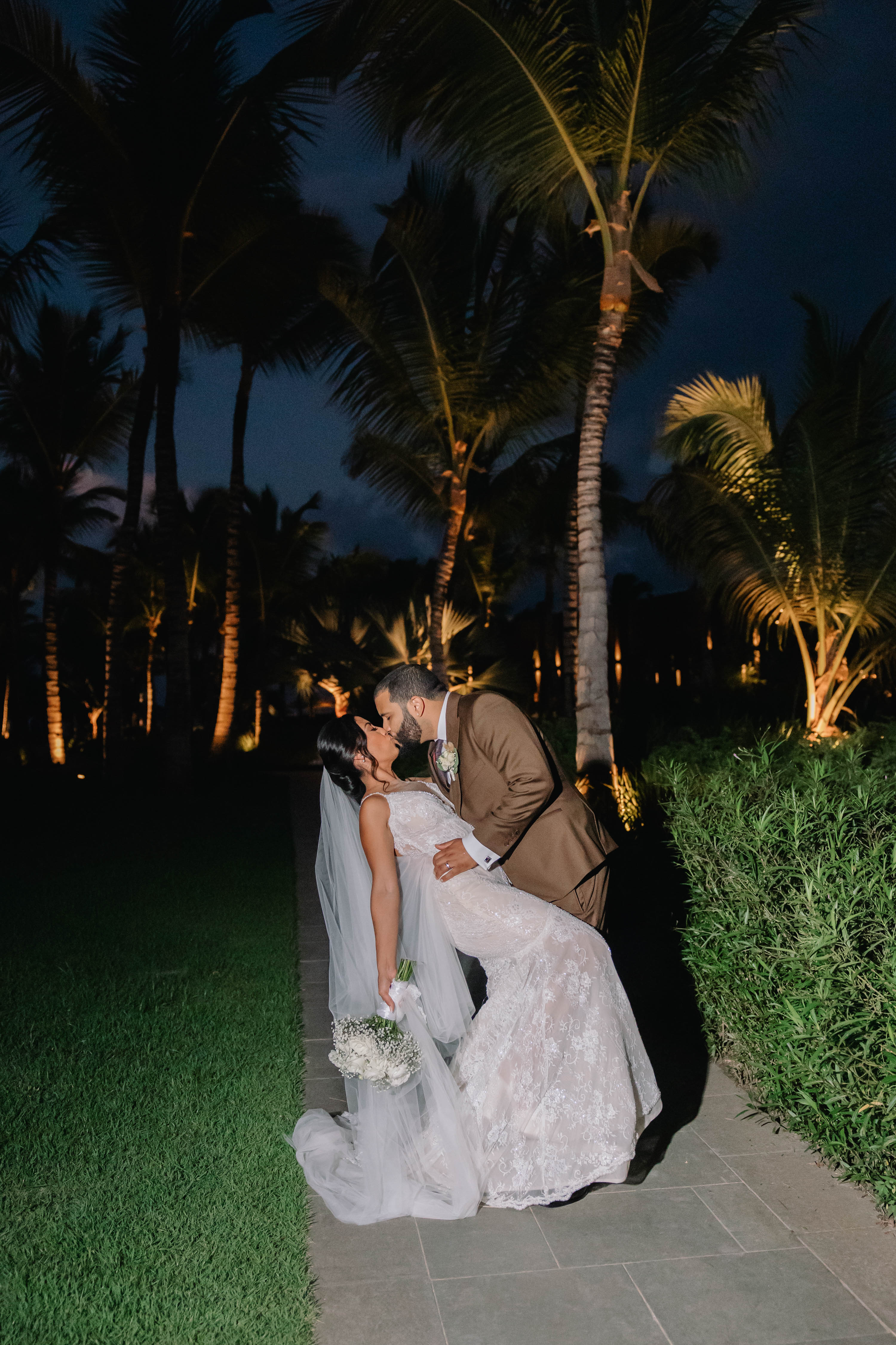 Couple embracing under palm trees at night. GL Bride Jennifer wearing our G-404
