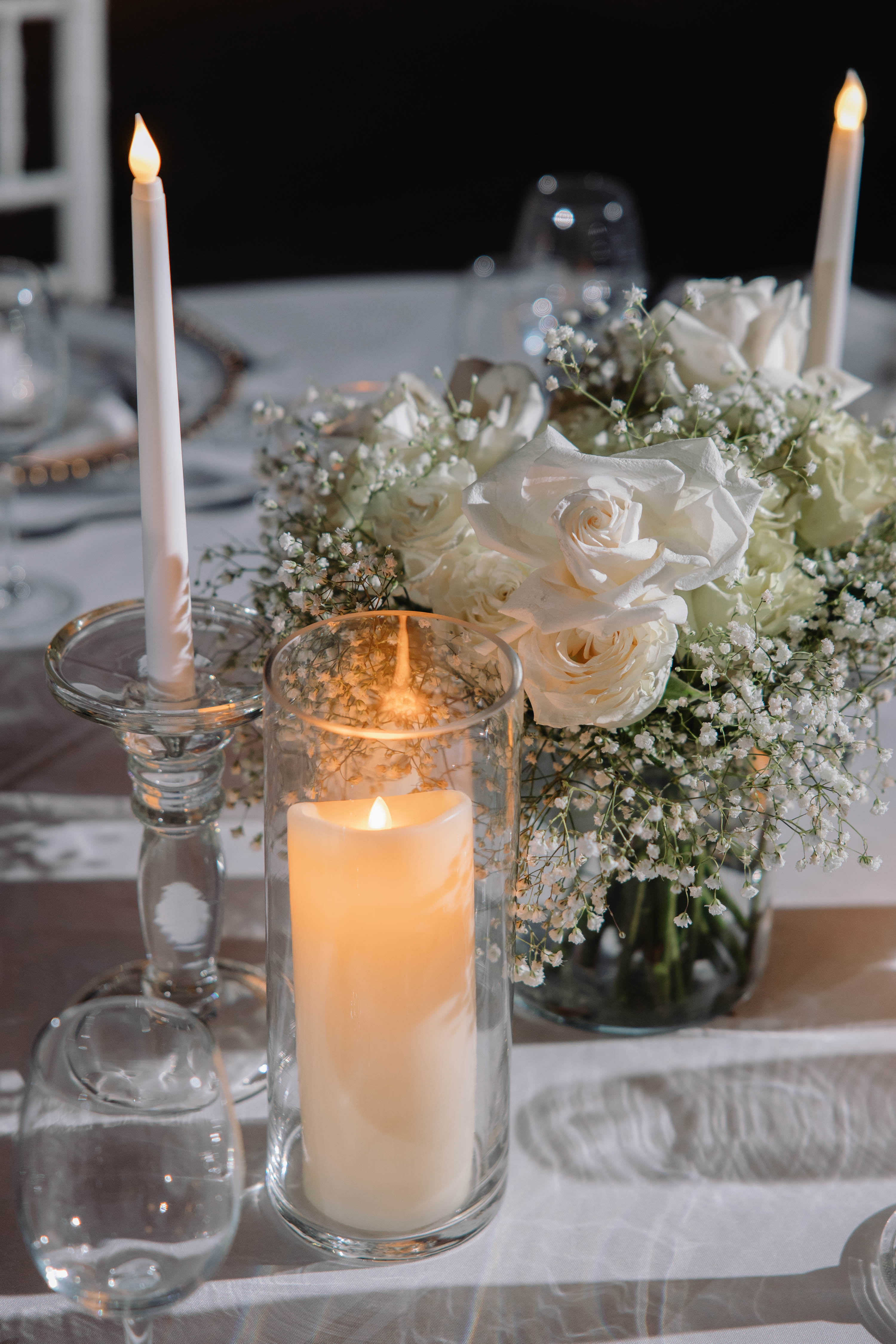 Decorative table setting with candles and flowers on a white tablecloth.