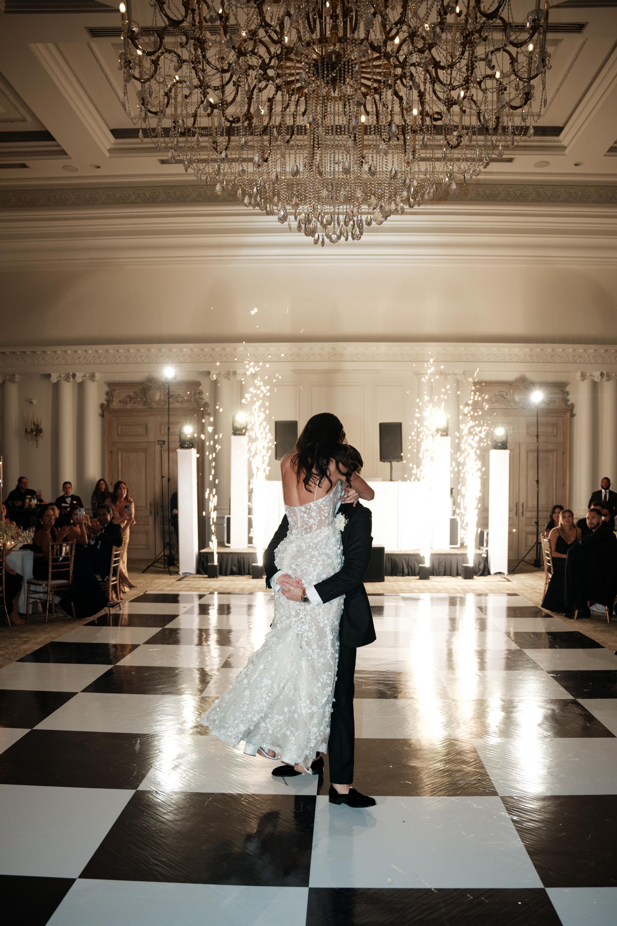 GL Bride Jessica wearing our Catalina gown and her husband dancing in a grand ballroom with chandeliers