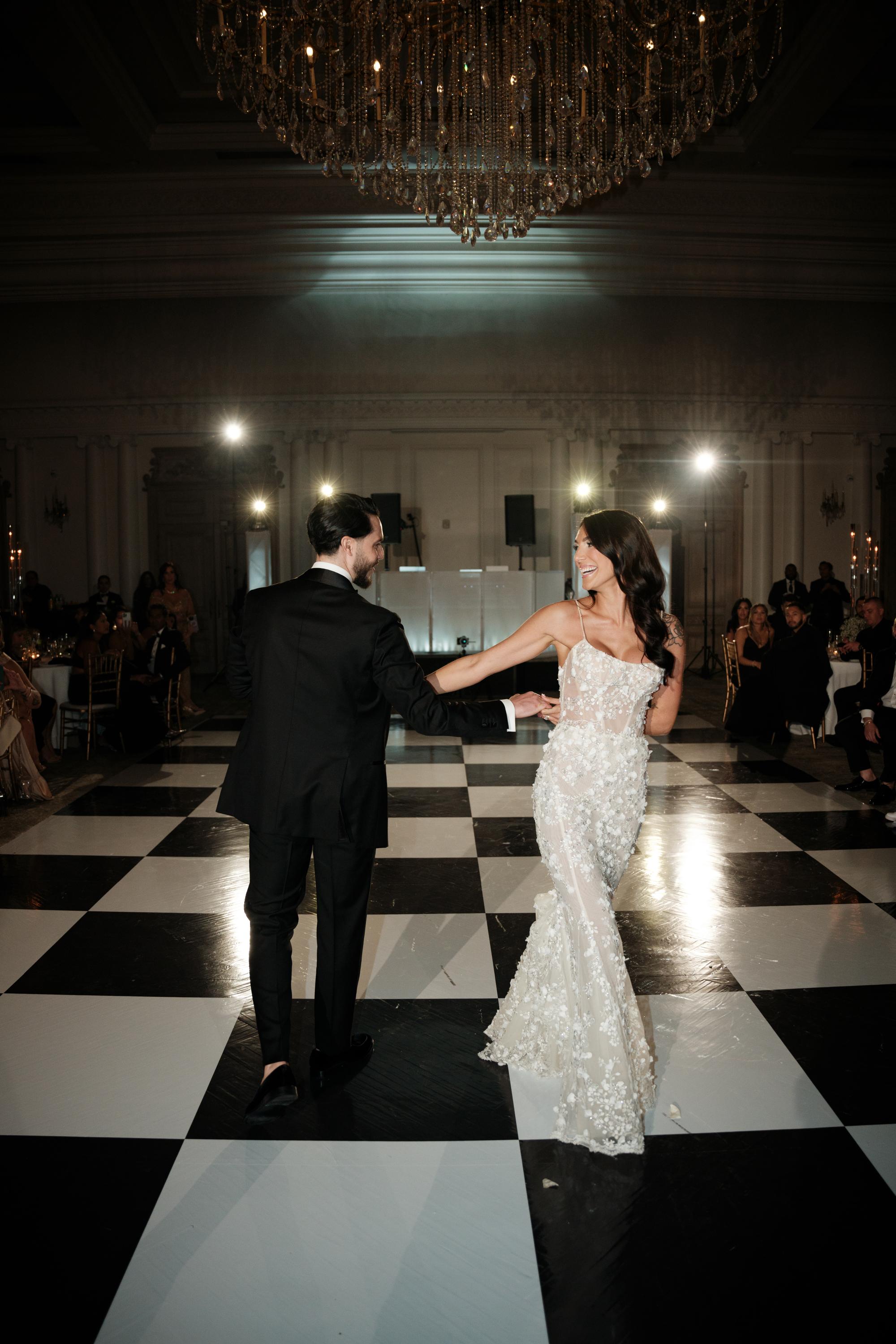 GL Bride Jessica wearing our Catalina gown  and her husband dancing on a black and white checkered floor in a formal setting.