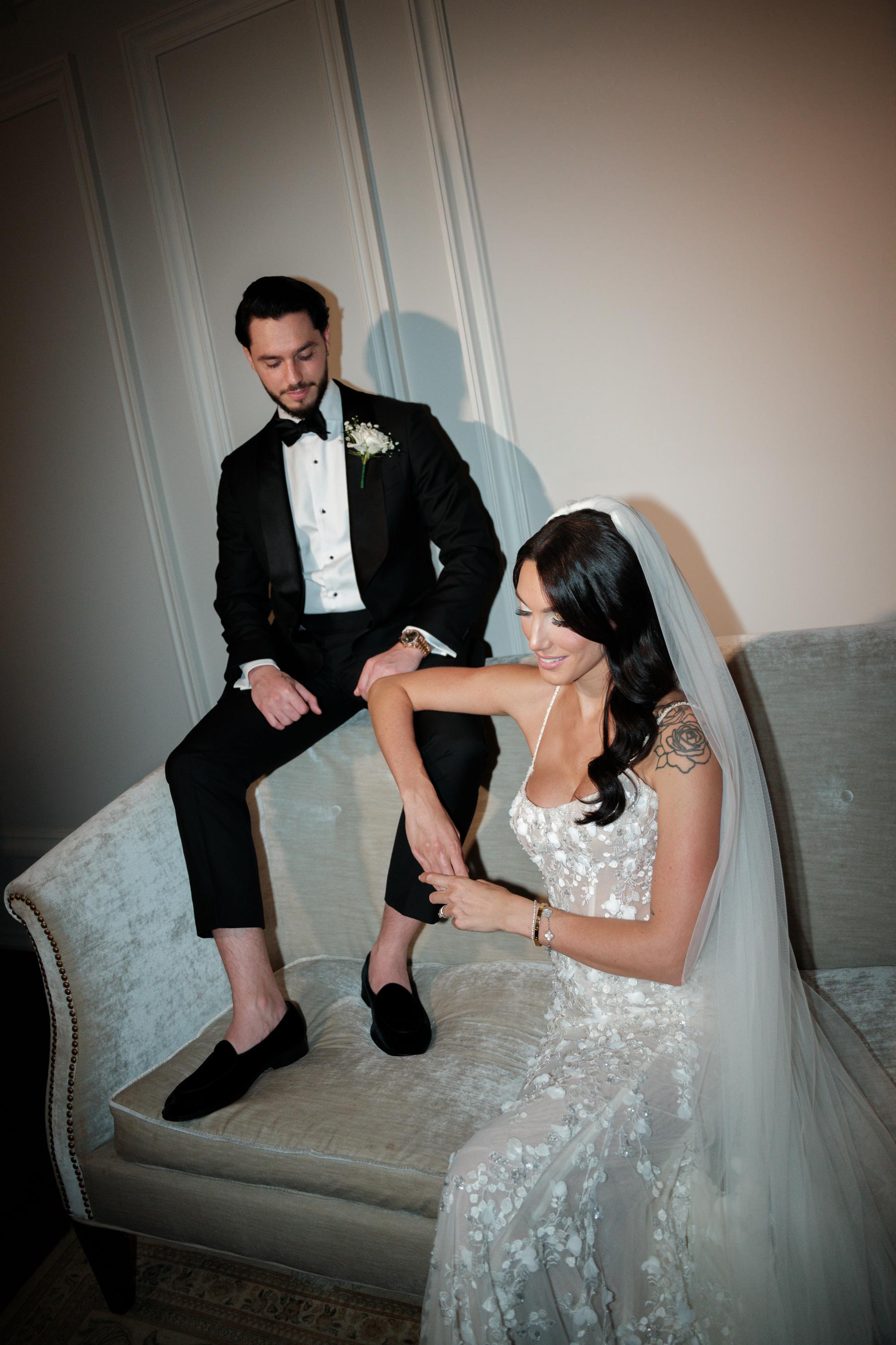 GL Bride Jessica wearing our Catalina gown and her husband sitting on a couch, likely post-wedding.