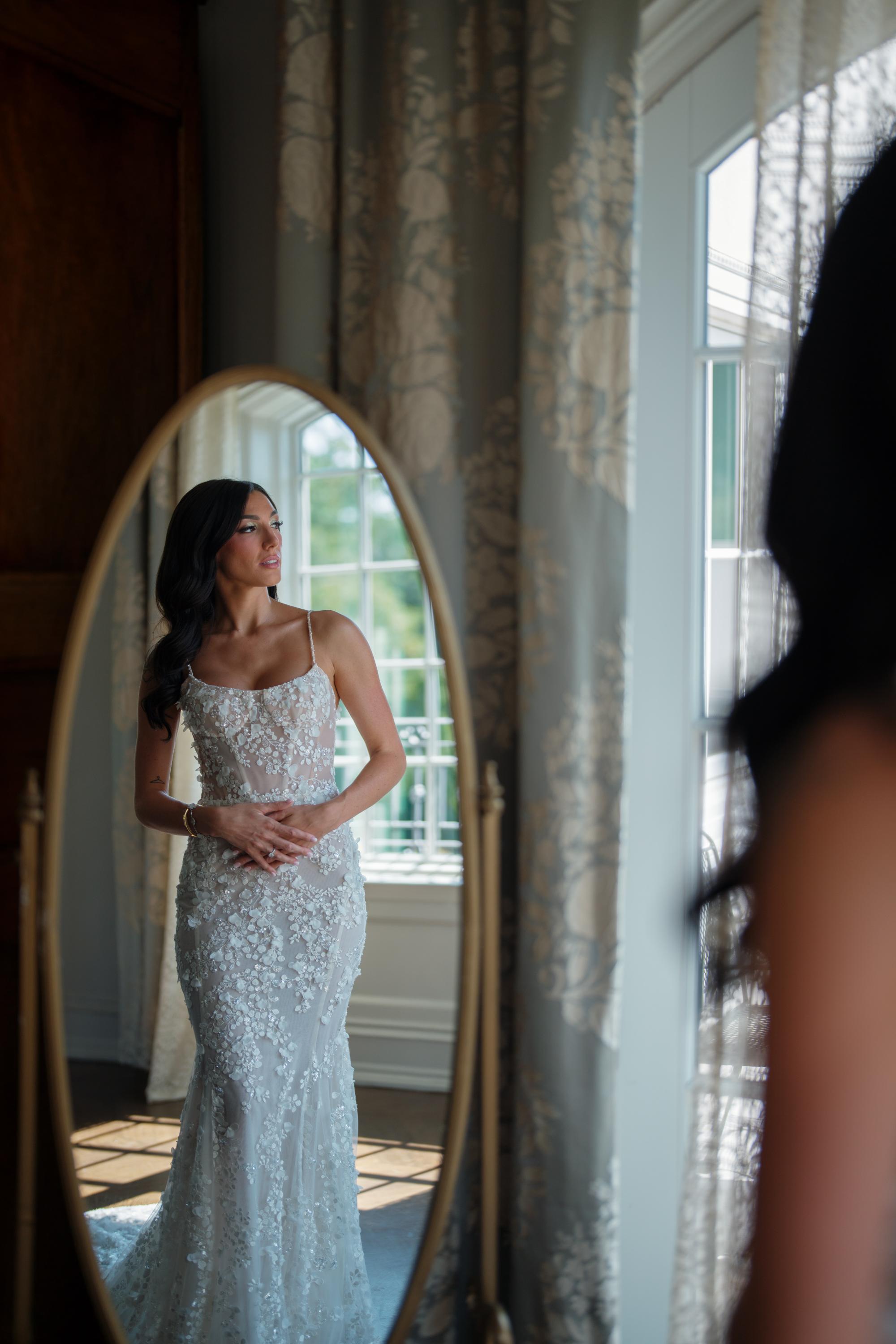 GL Bride Jessica wearing our Catalina gown, standing in front of a mirror.