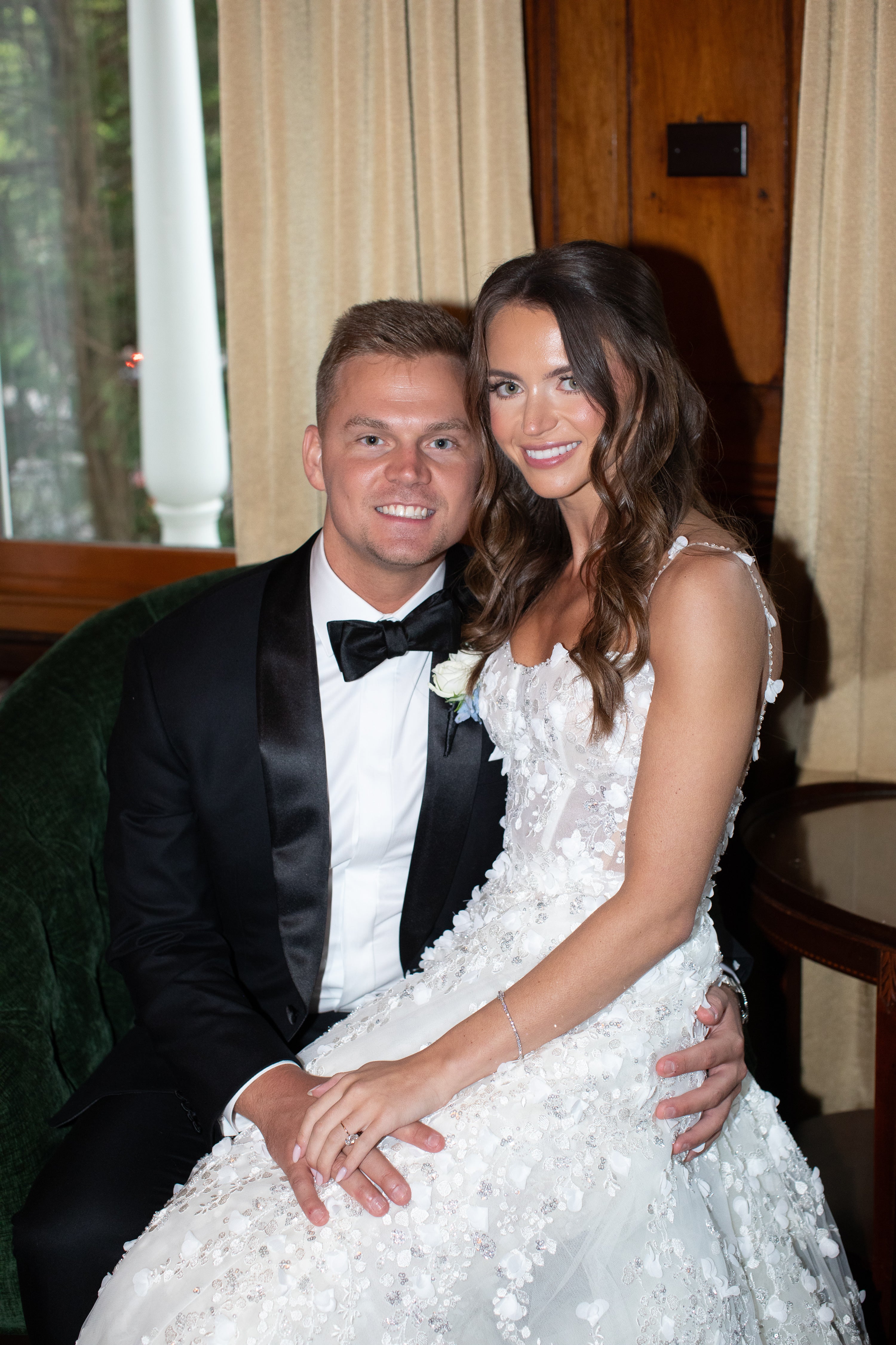 Man in a tuxedo and woman in a white dress sitting together, possibly at an event.
