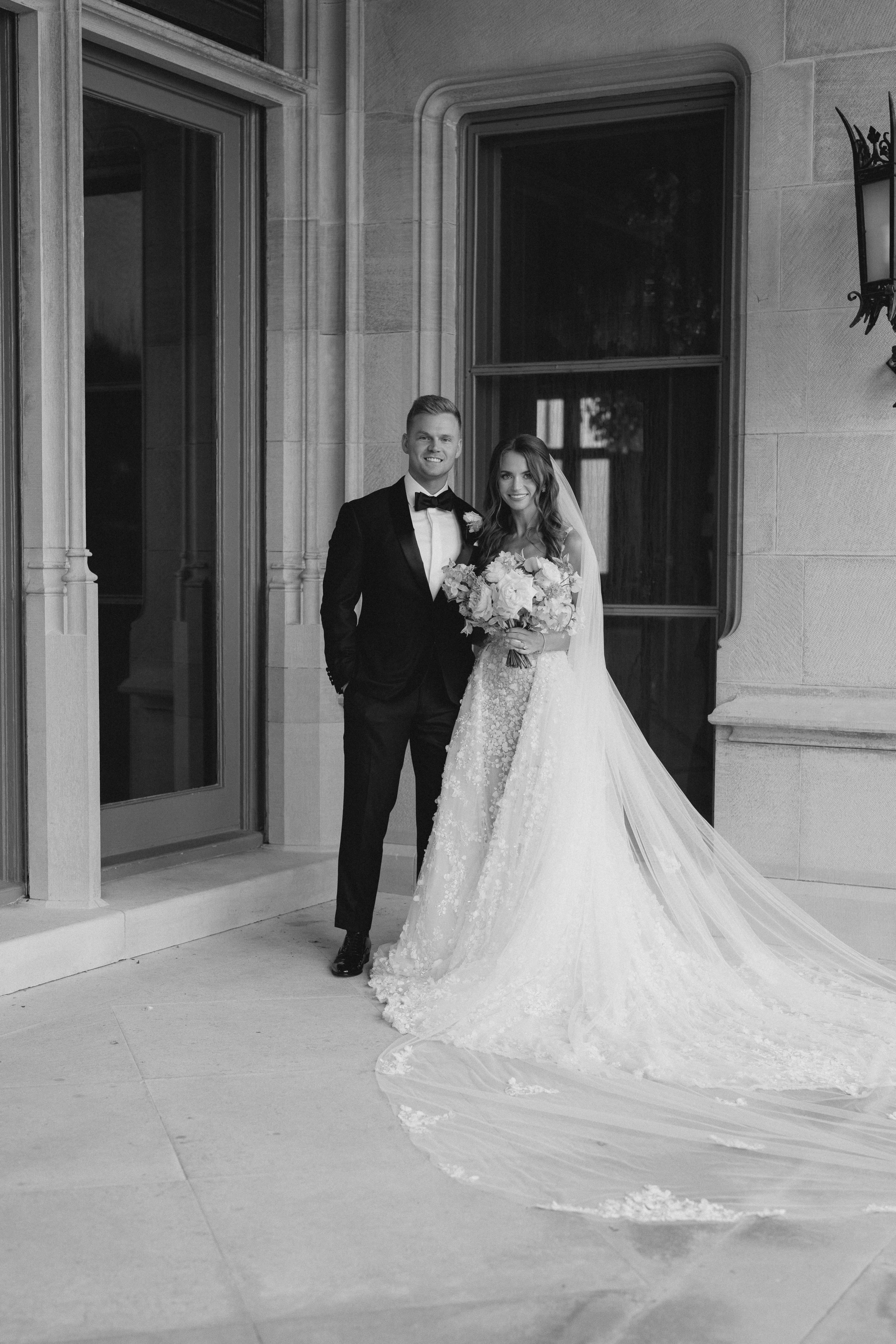 Black and white photo of a bride and groom standing in front of a building.