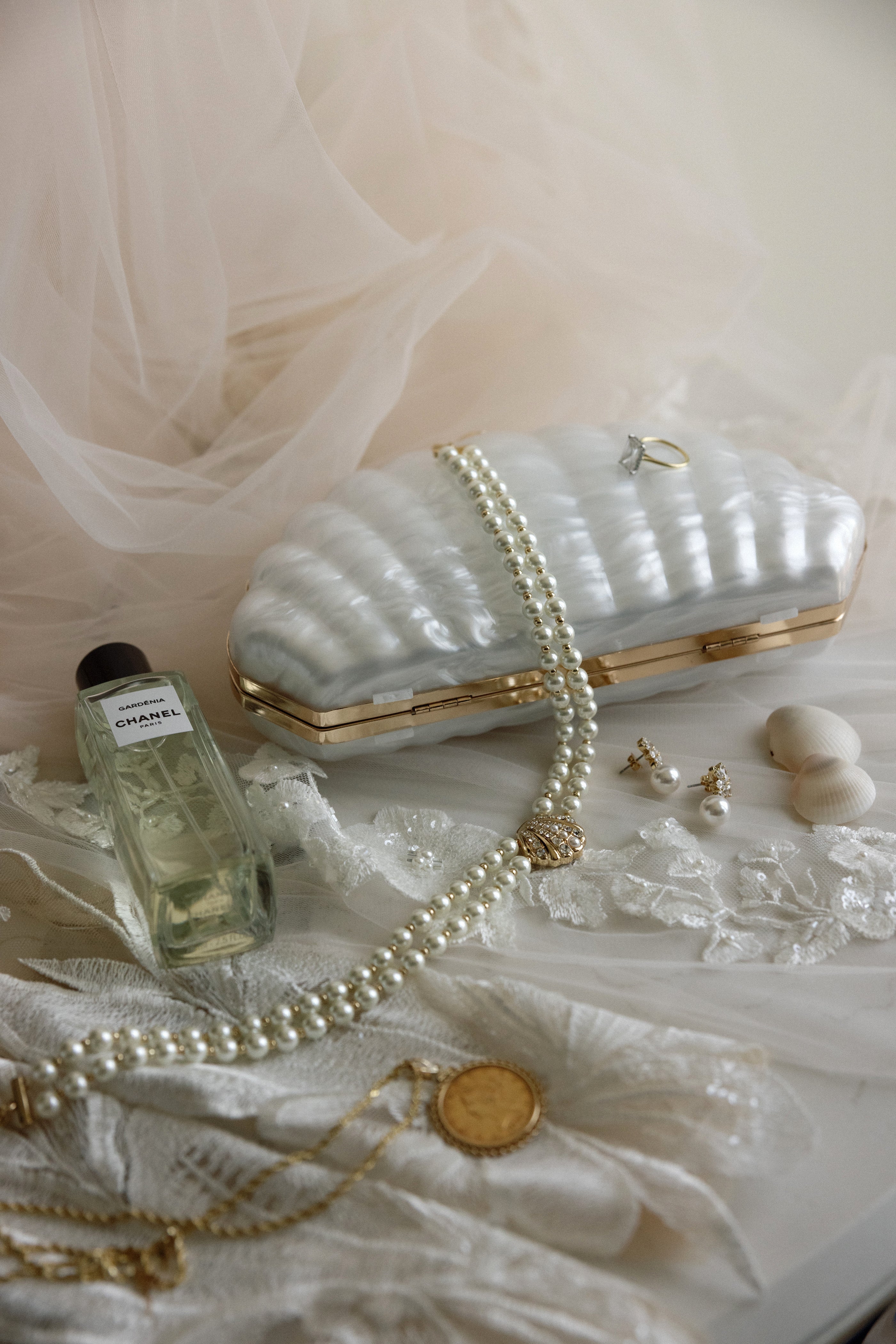 White handbag with gold accents, pearl necklace, earrings, and perfume bottle on a white fabric background