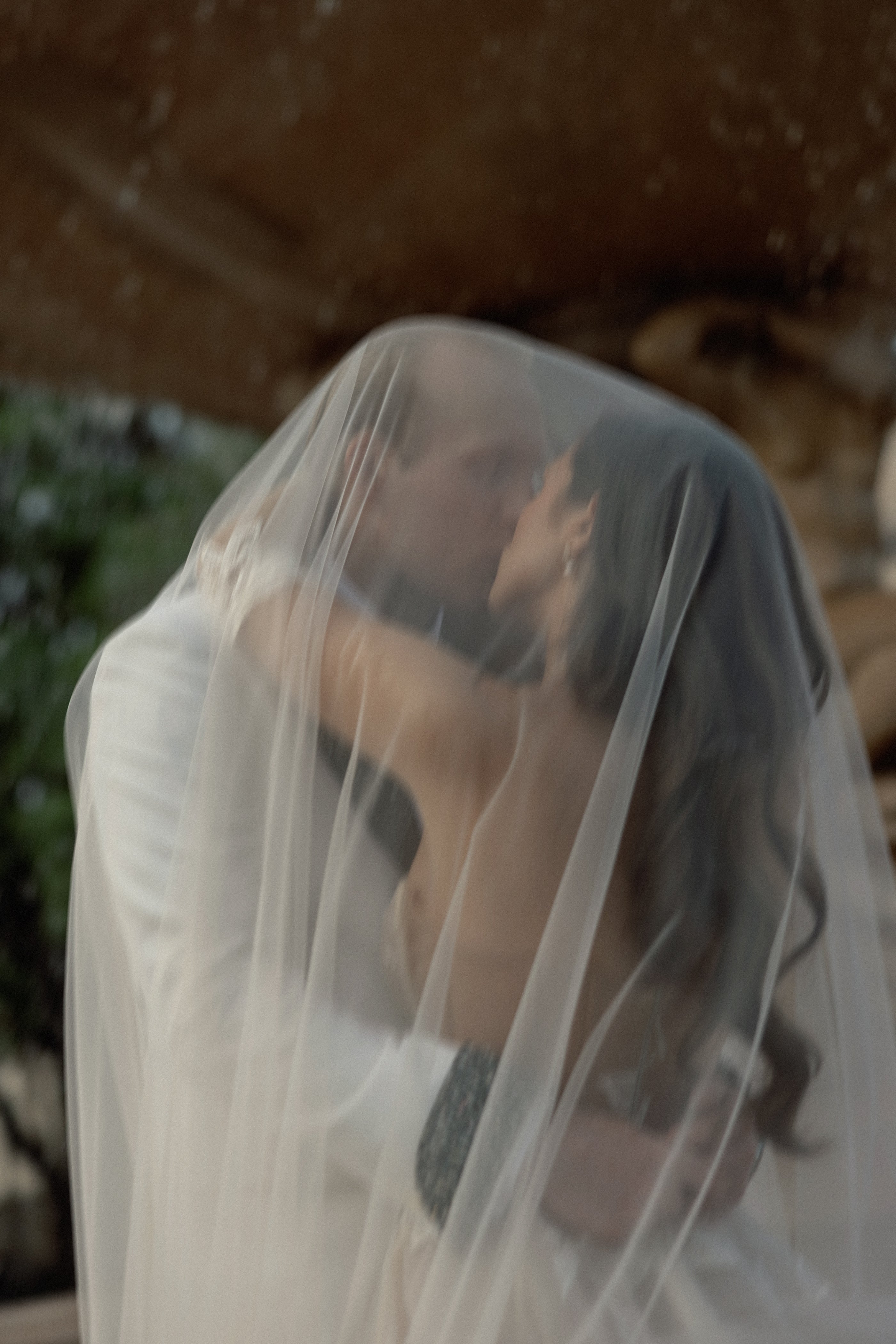 Two people embracing under a veil with a blurred natural background