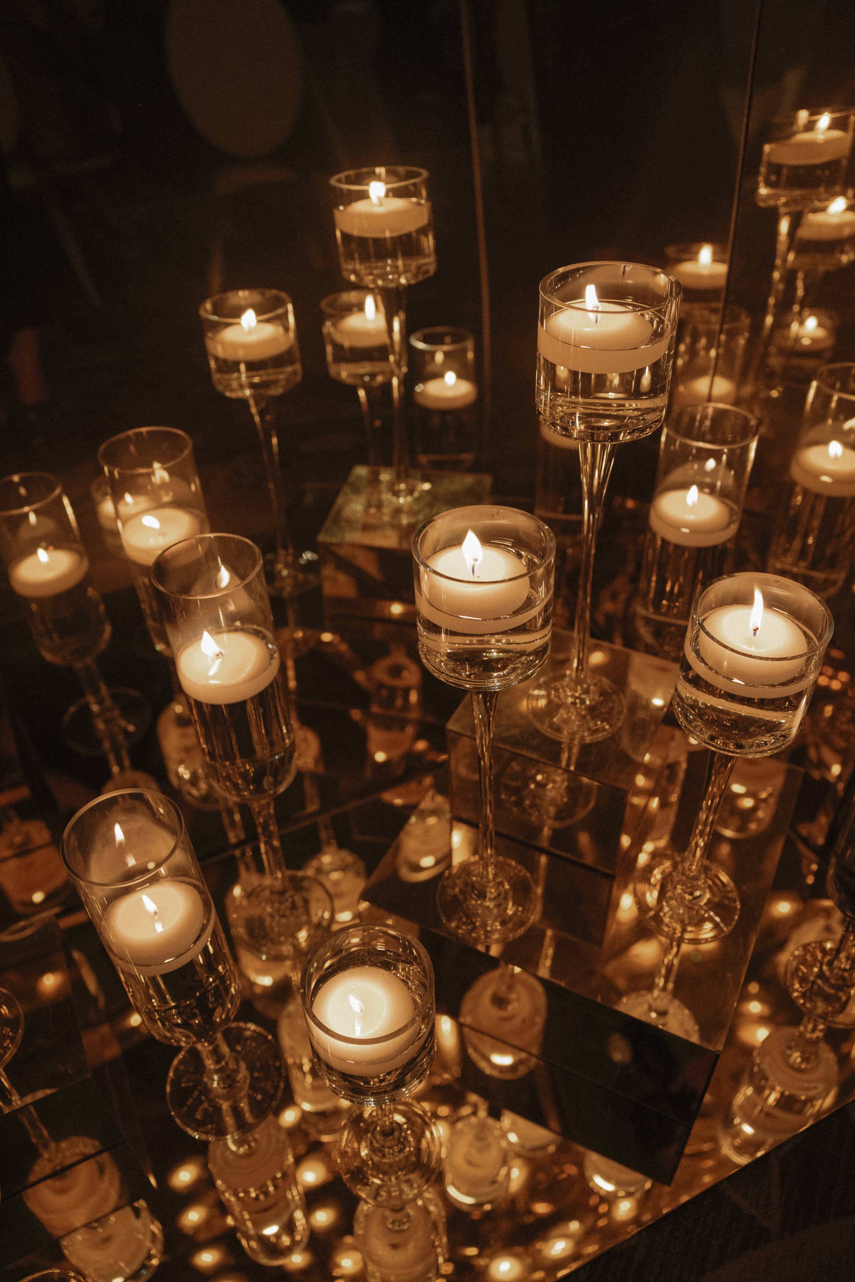 Decorative candles in glass holders on a reflective surface with a dark background