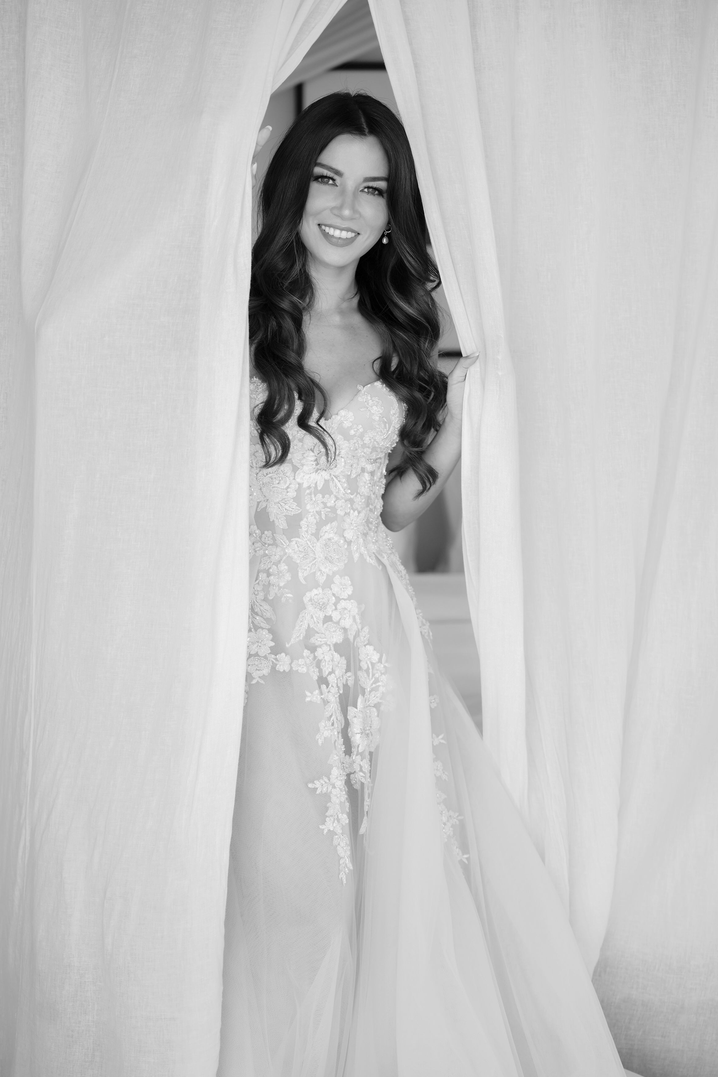 Woman in a wedding dress standing behind sheer curtains