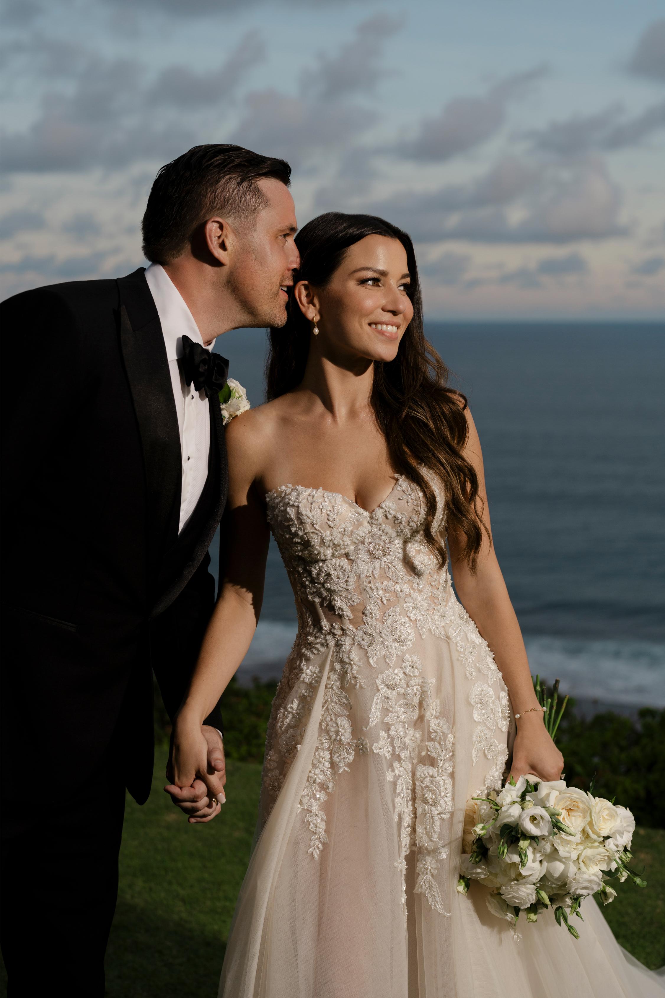 Man and woman in wedding attire standing by the ocean