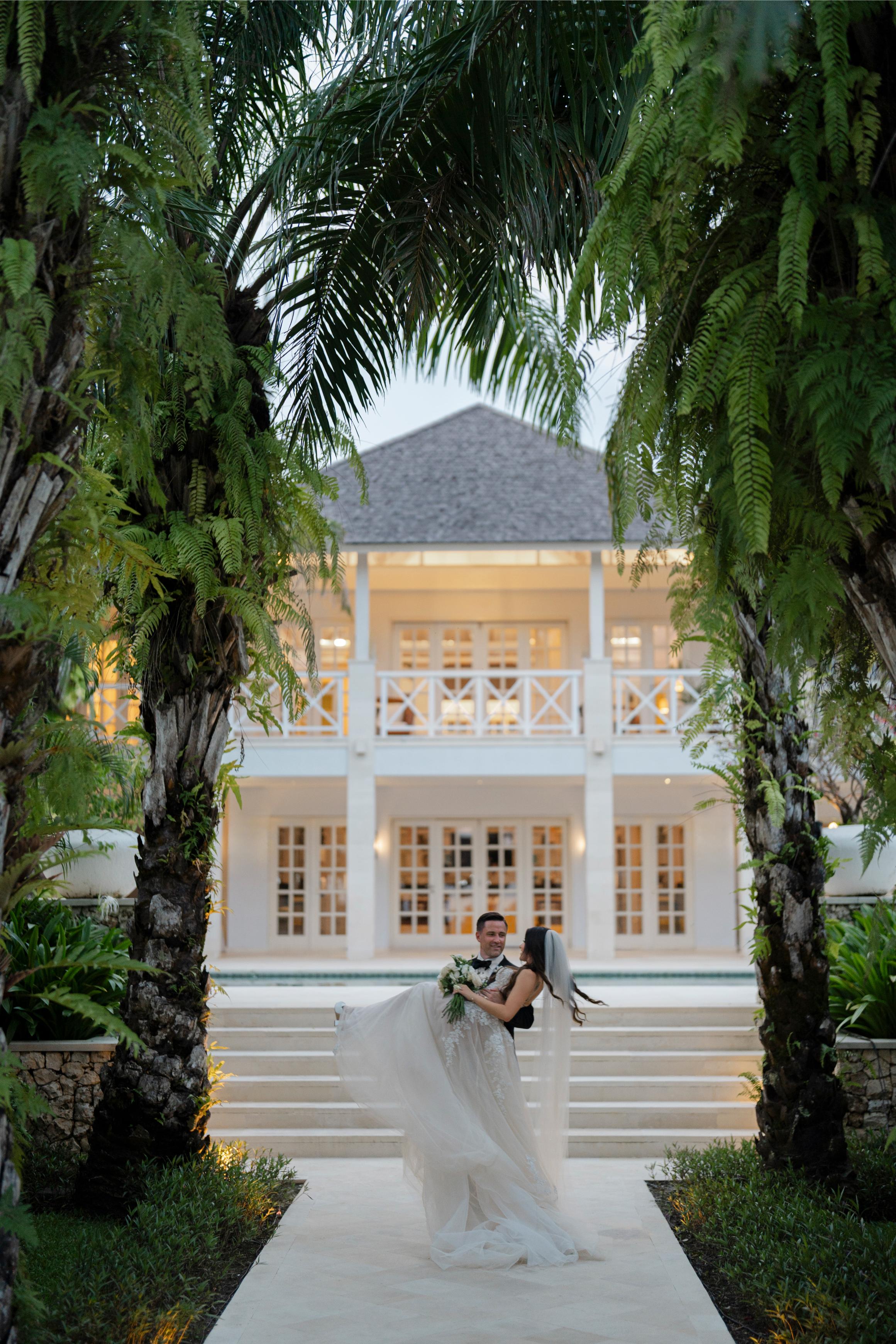 Tropical wedding scene with a couple in front of a white house.