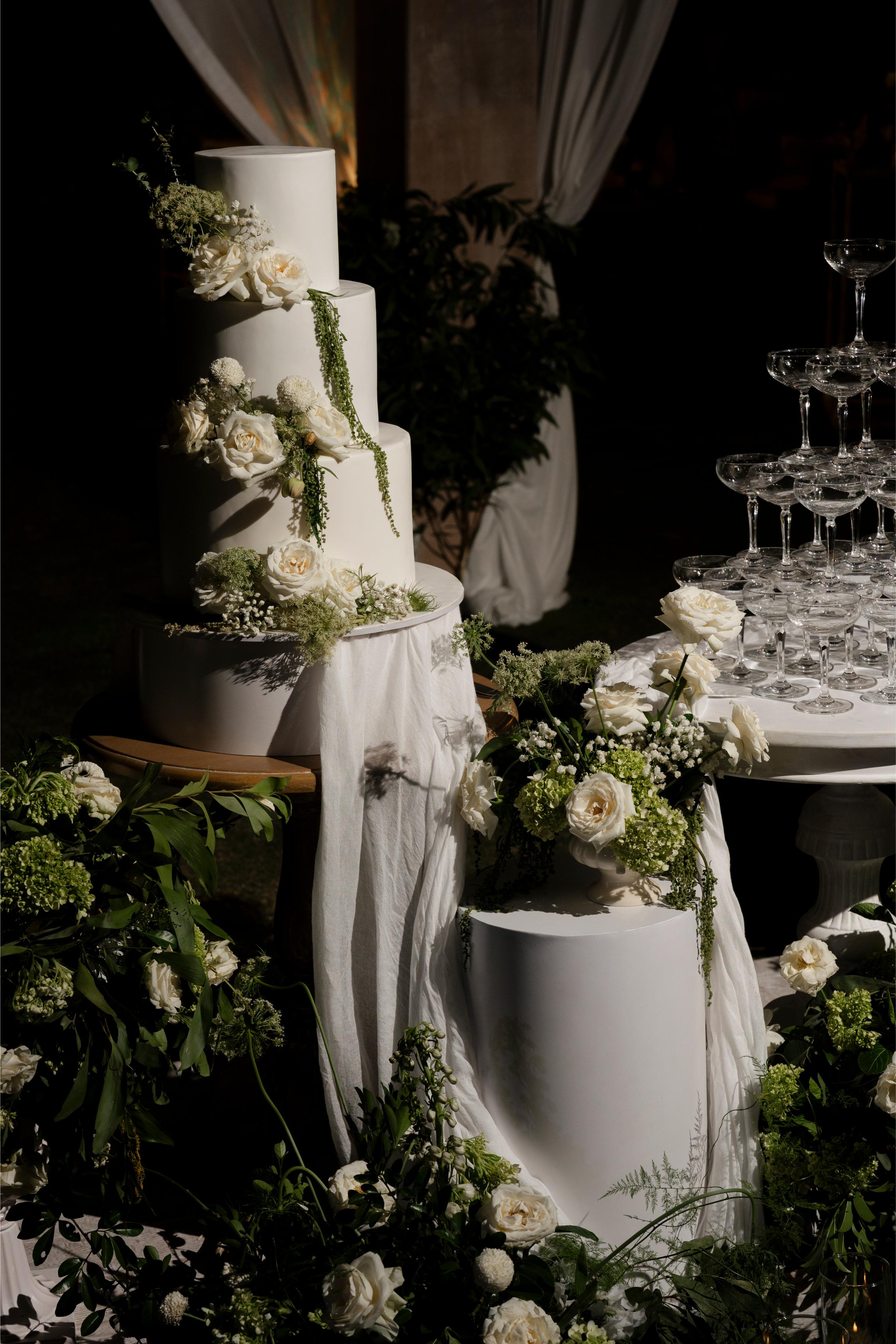 Decorative wedding cake with floral arrangements and a crystal stand in a dark setting