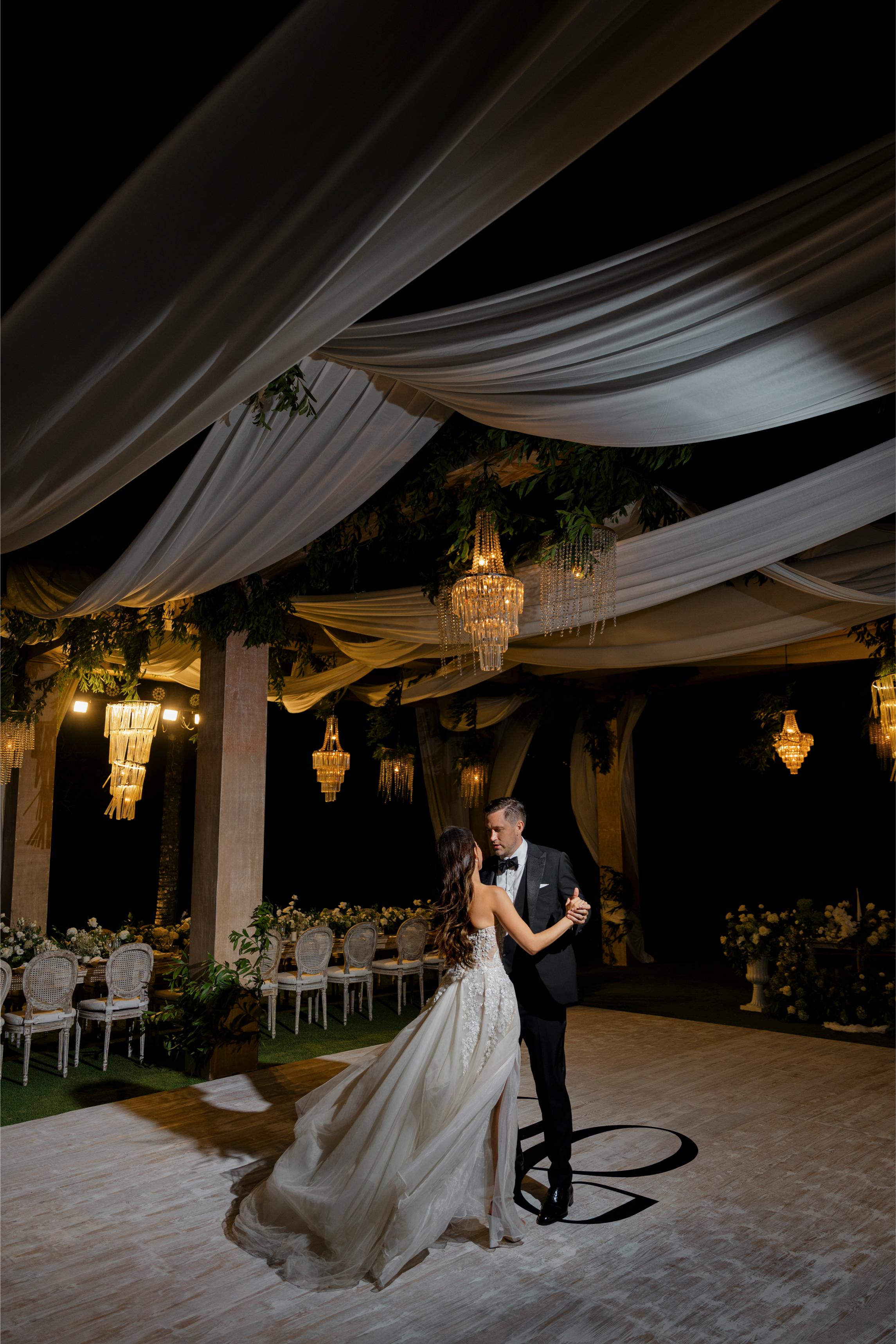 Wedding couple dancing under a decorated ceiling with chandeliers.