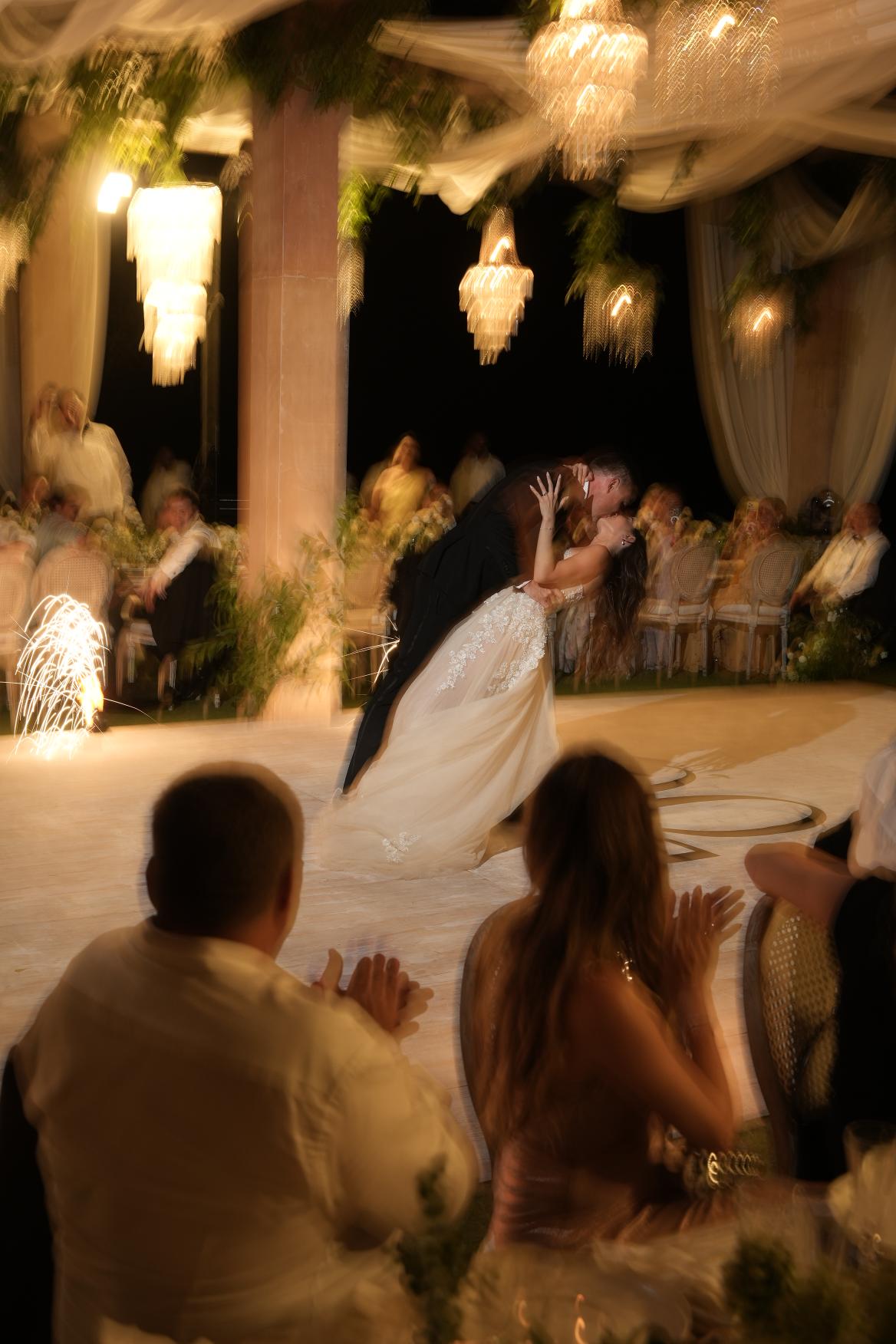 Wedding couple under a decorated archway with guests in the background.