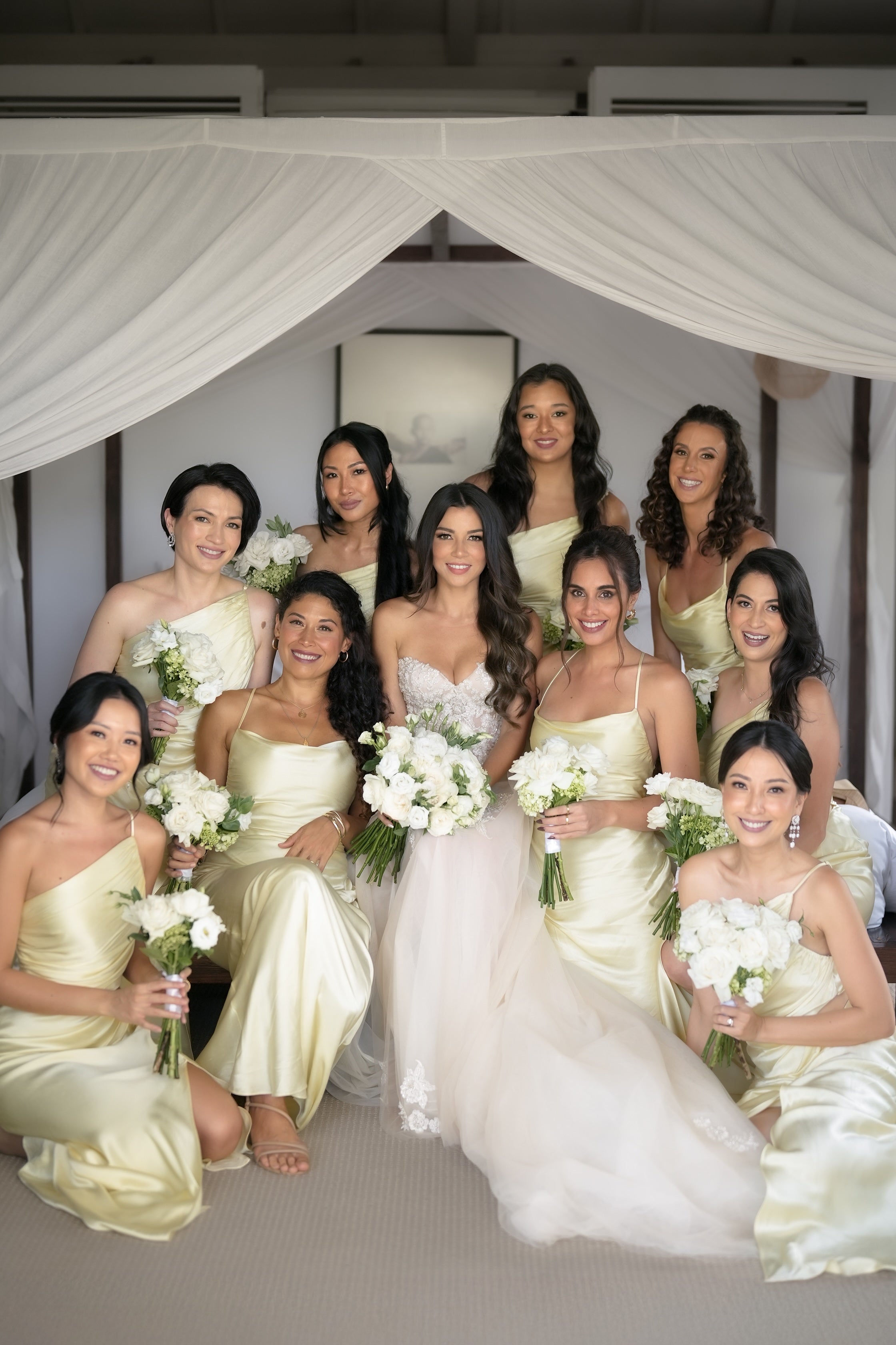 Group of women in formal dresses with floral bouquets indoors.