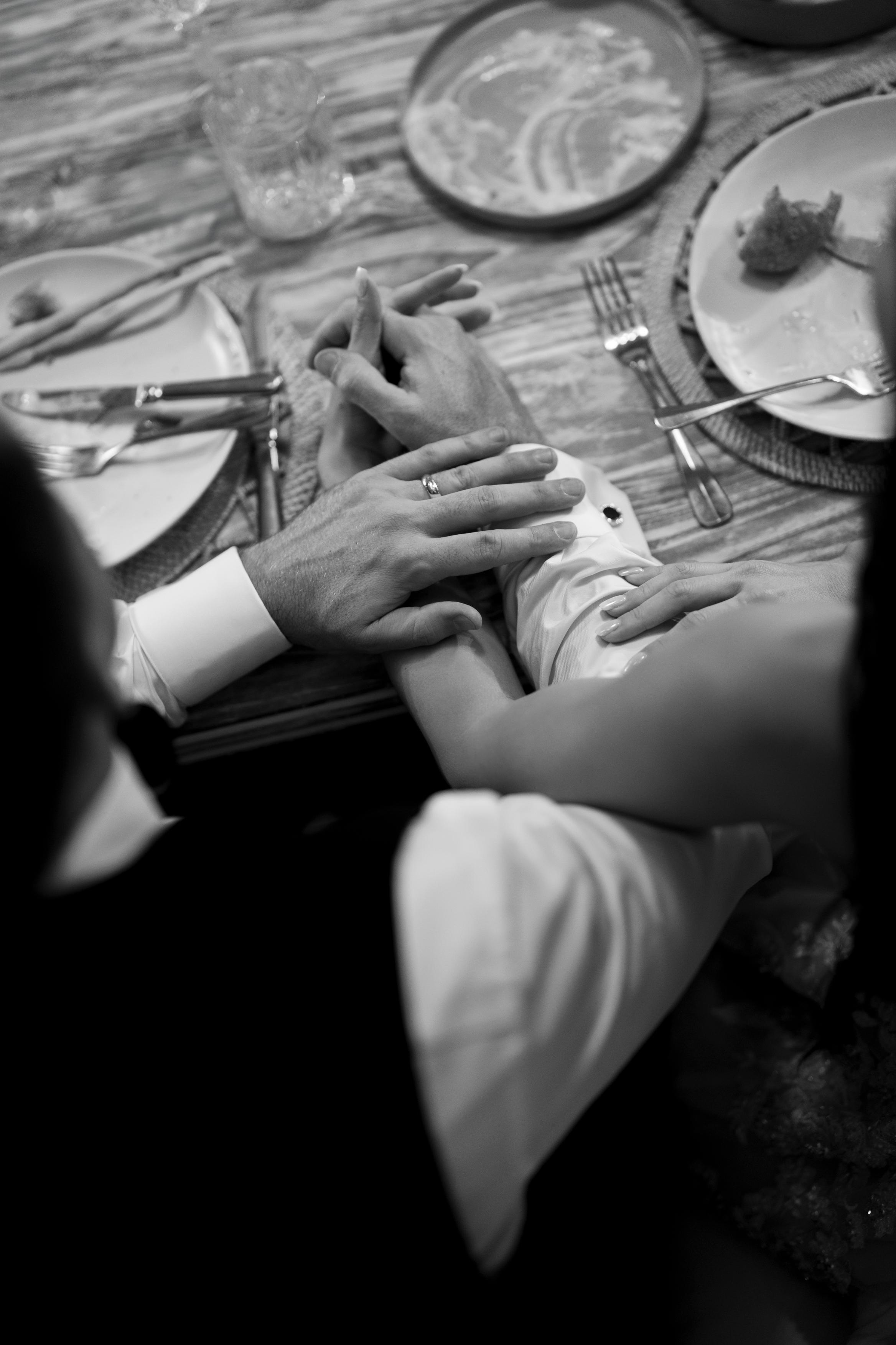Two people holding hands at a table with a ring on one hand, in a black and white photo.