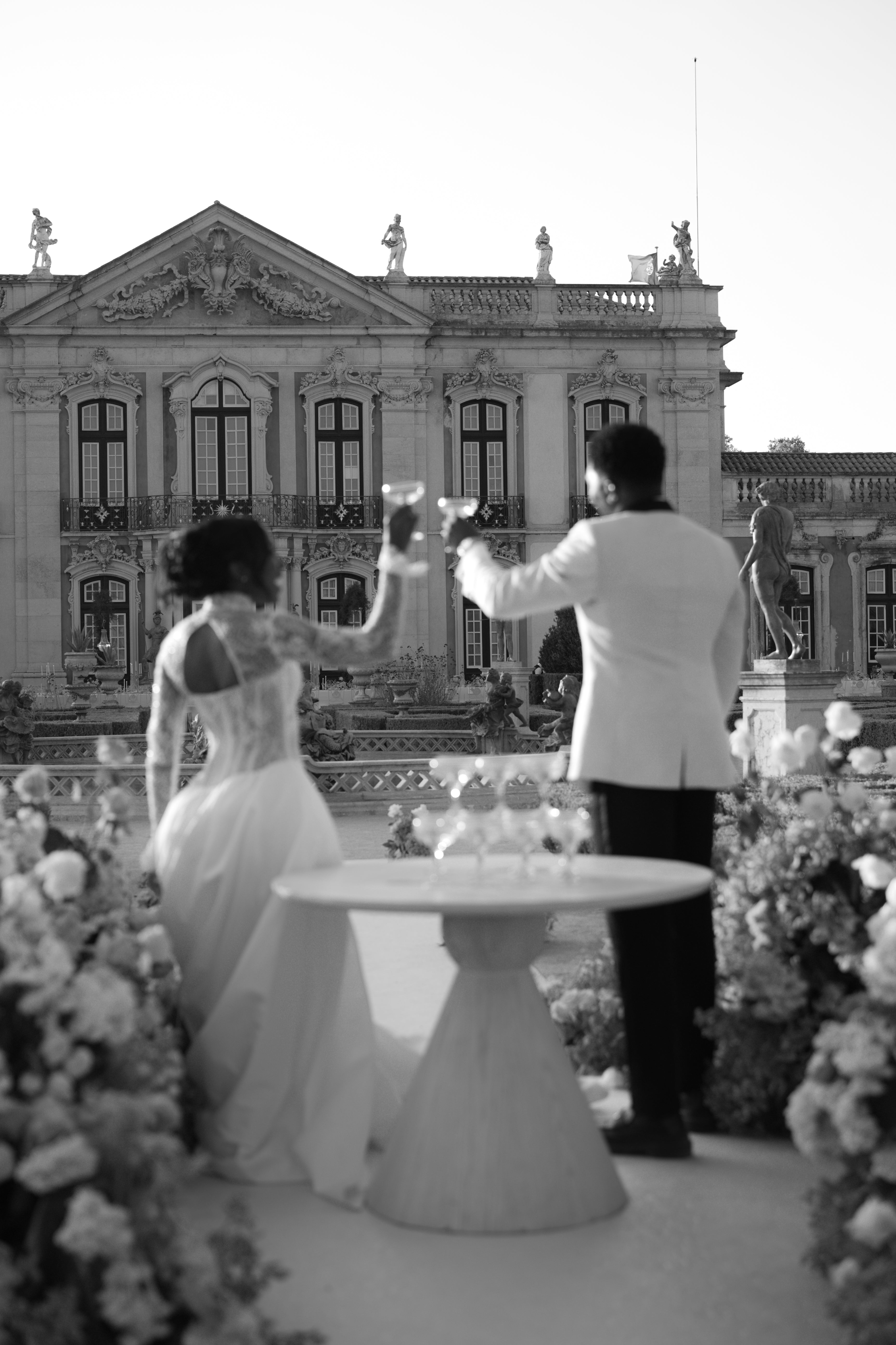 Couple raising glasses in front of an ornate building with floral decorations.